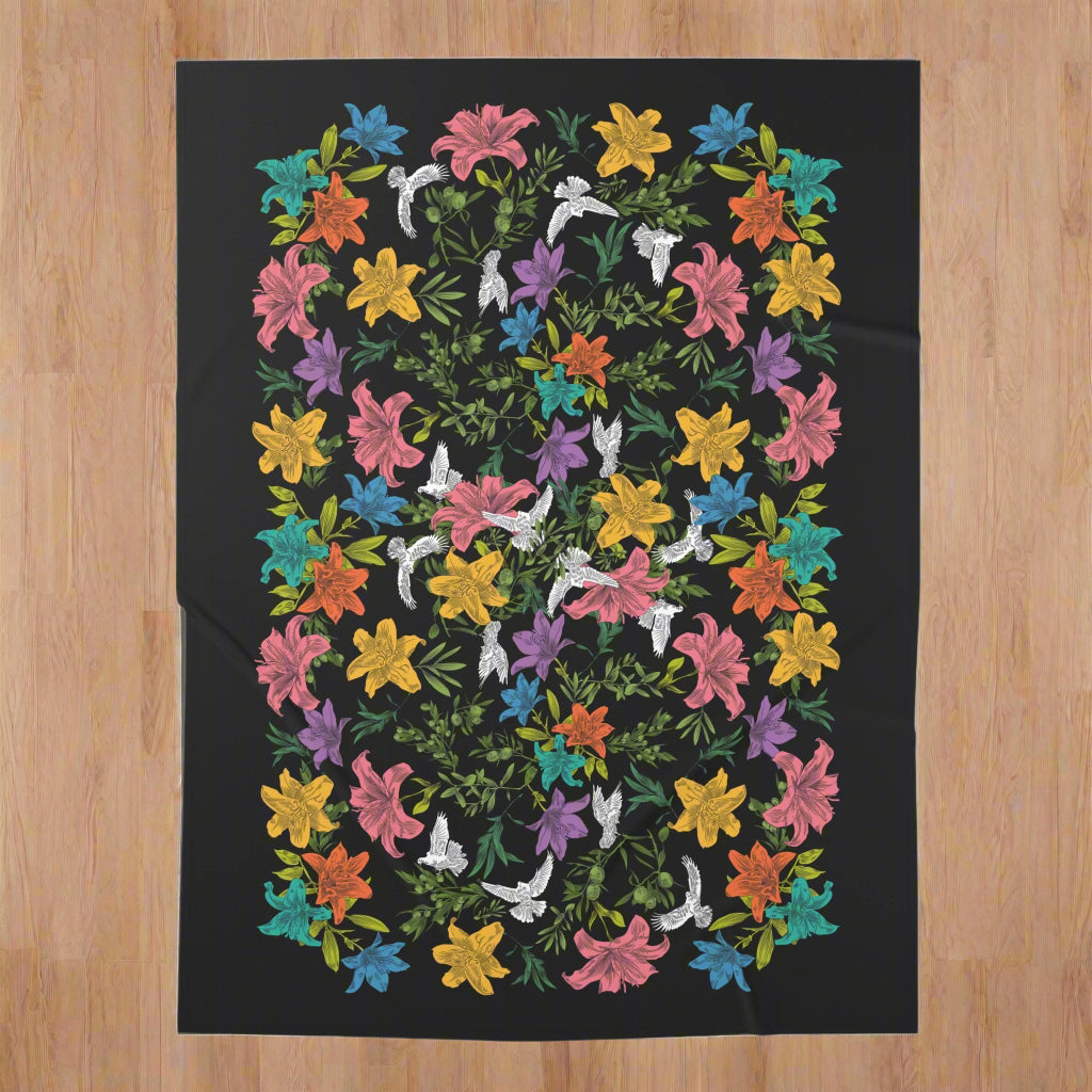 An overhead view of a black swaddle blanket with an all-over, multi-colored pattern of doves, flowers, and olive branches.