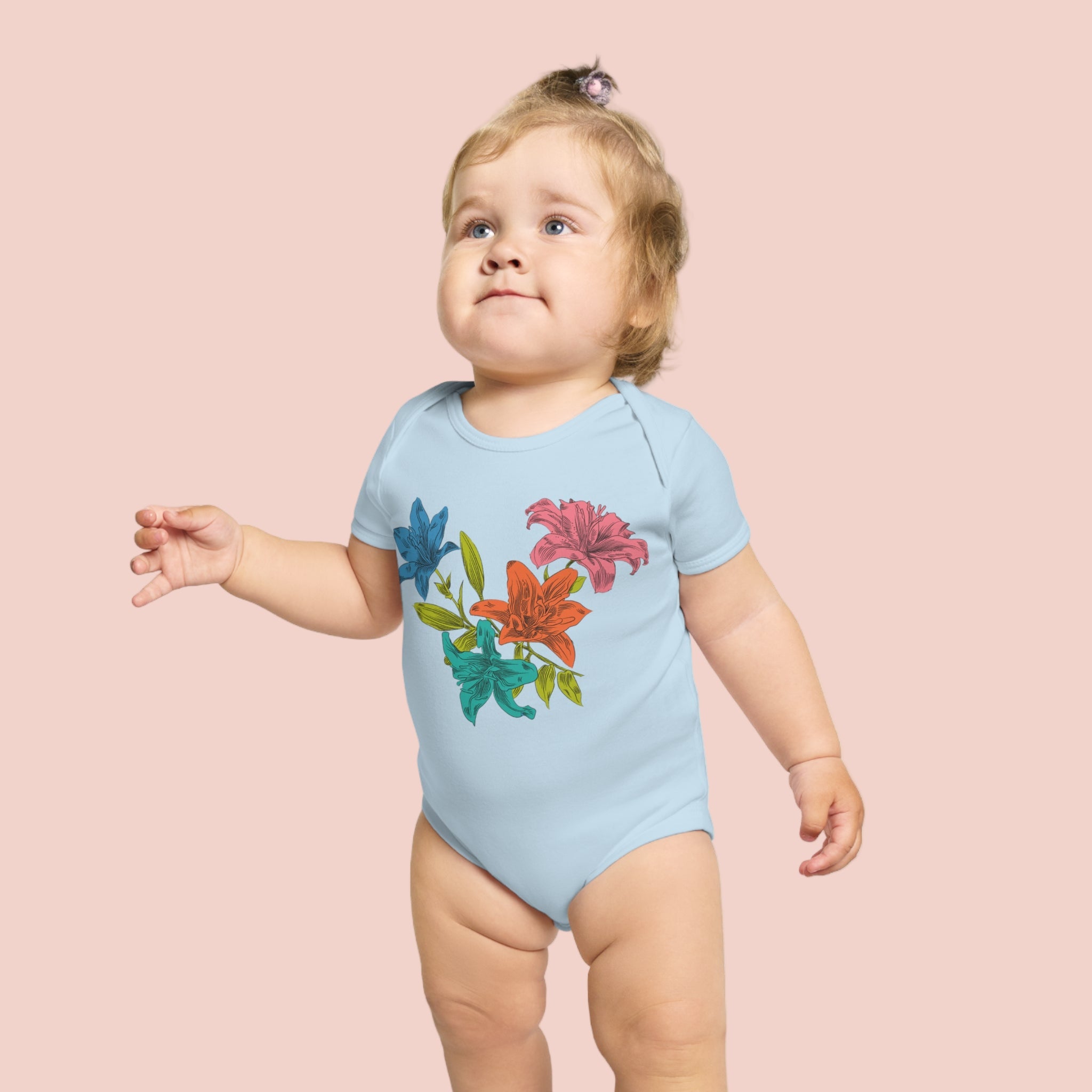 Child wearing a light blue onesie with colorful floral designs on a pale pionk background