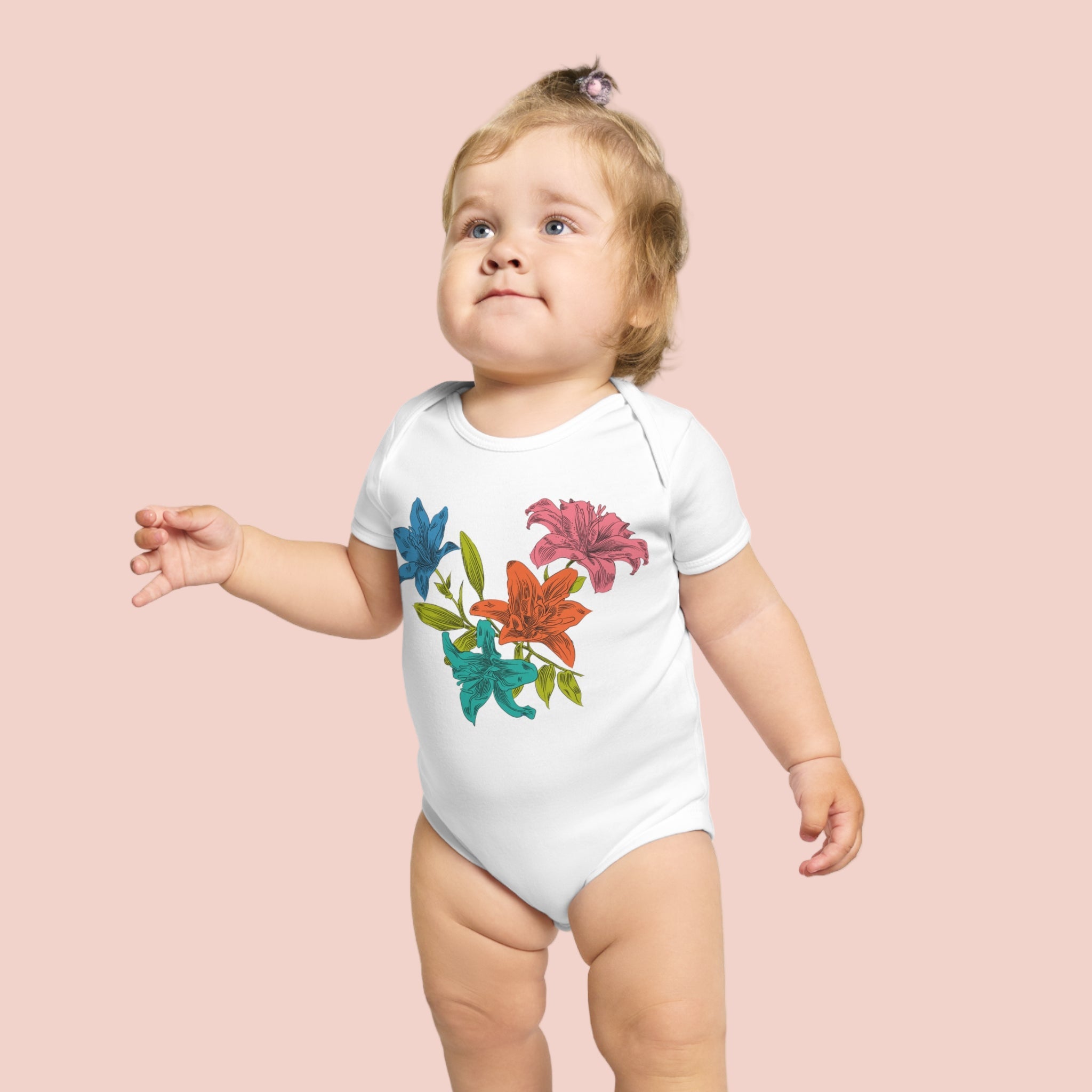 Baby wearing a white onesie with colorful floral designs on a pale background