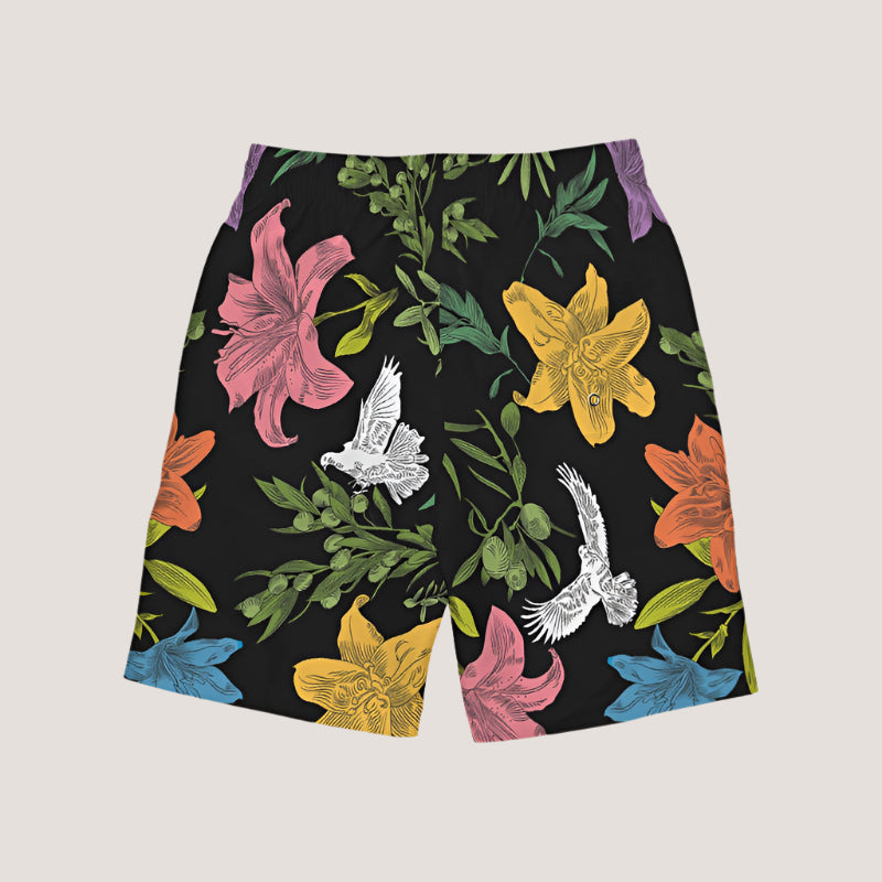 Back angle of black board shorts with an all-over, multi-colored pattern of flowers, olive branches, and doves, has white external ties and elastic waistband.