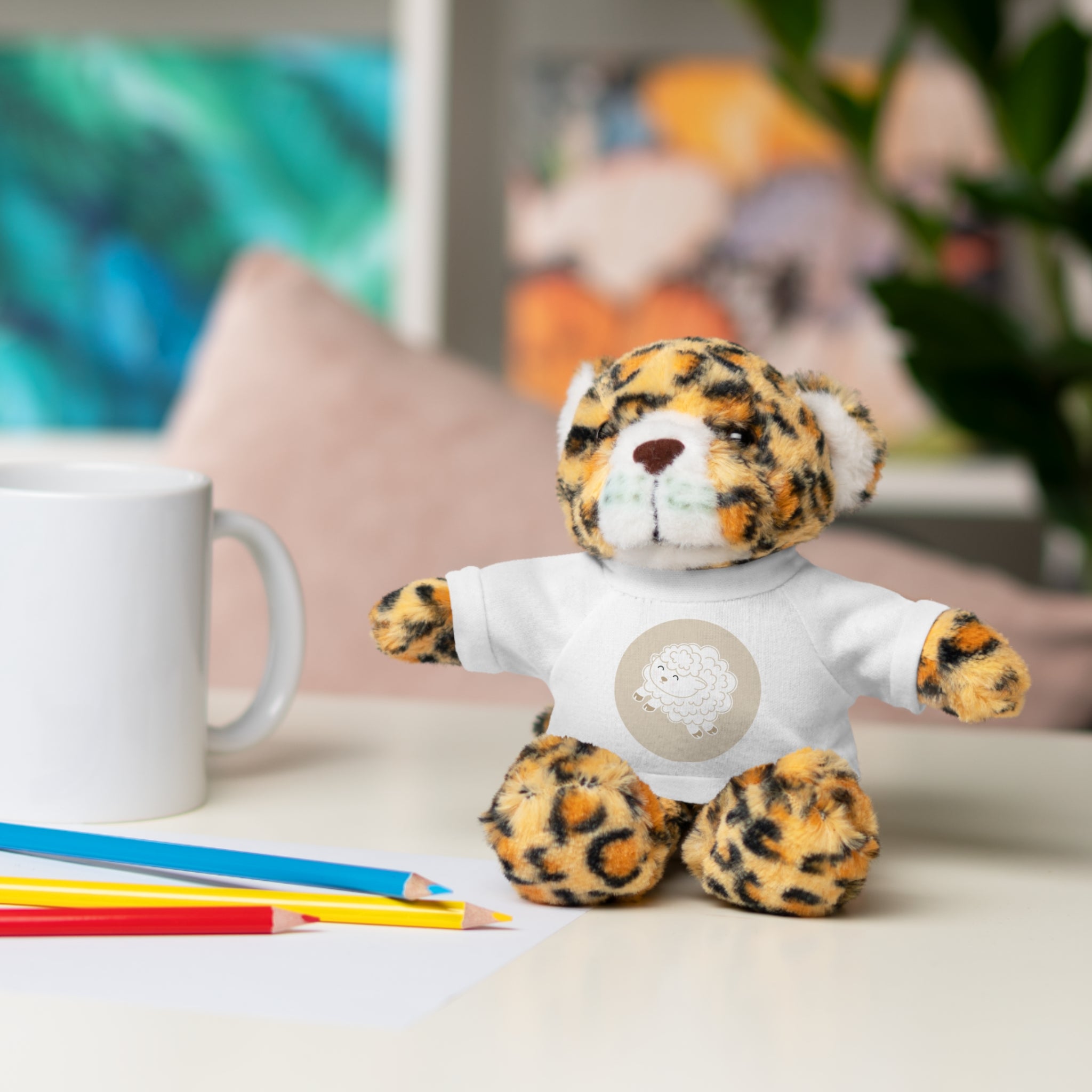 Leopard print plushie wearing a white shirt with a lamb graphic design on a desk with stationery items.