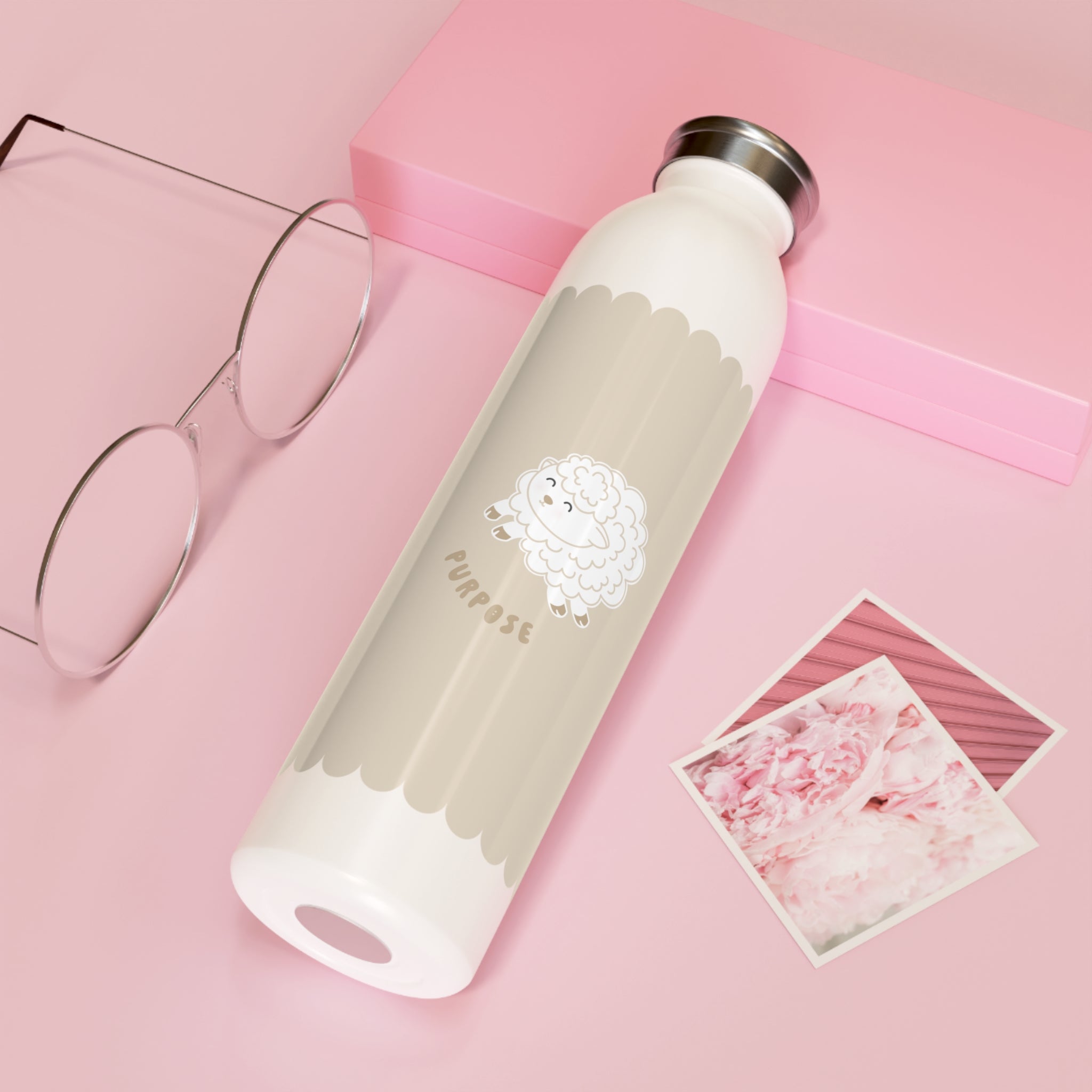 A white insulated water bottle with a silver cap and a beige scalloped label featuring a lamb illustration and the word 'purpose', styled on a pink background with eyeglasses, pink box, and two photo cards.
