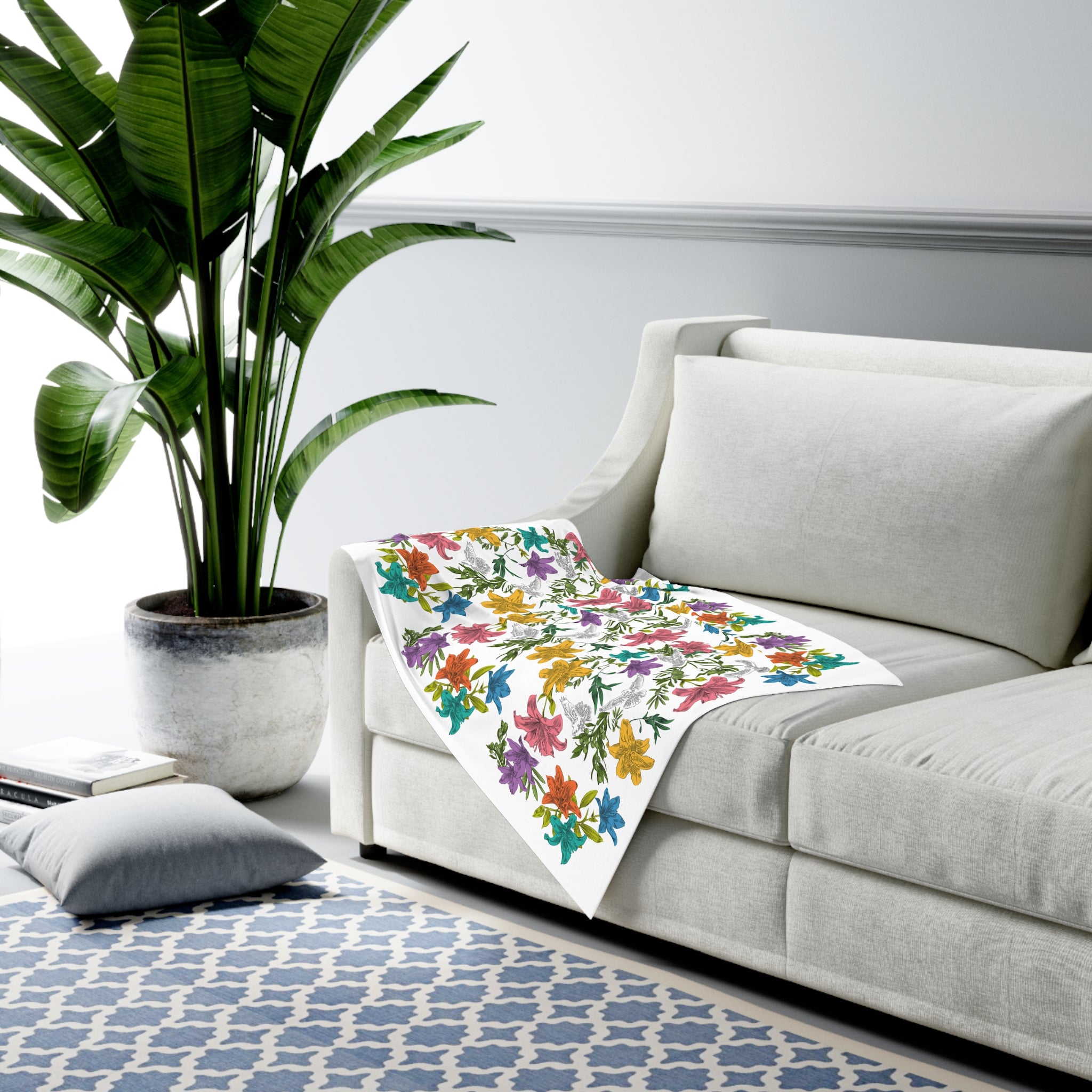 Colorful floral and dove blanket on a gray sofa with a plant and rug in a living room setting
