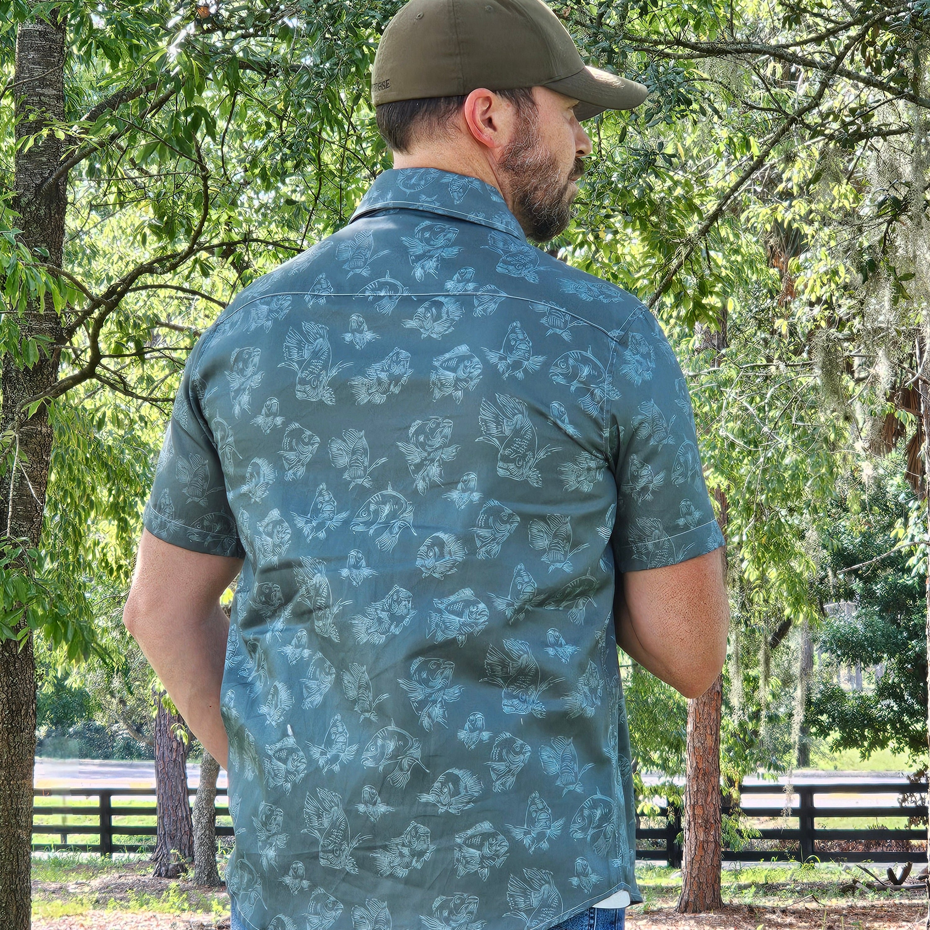 Man wearing a patterned shirt and cap in a forest setting