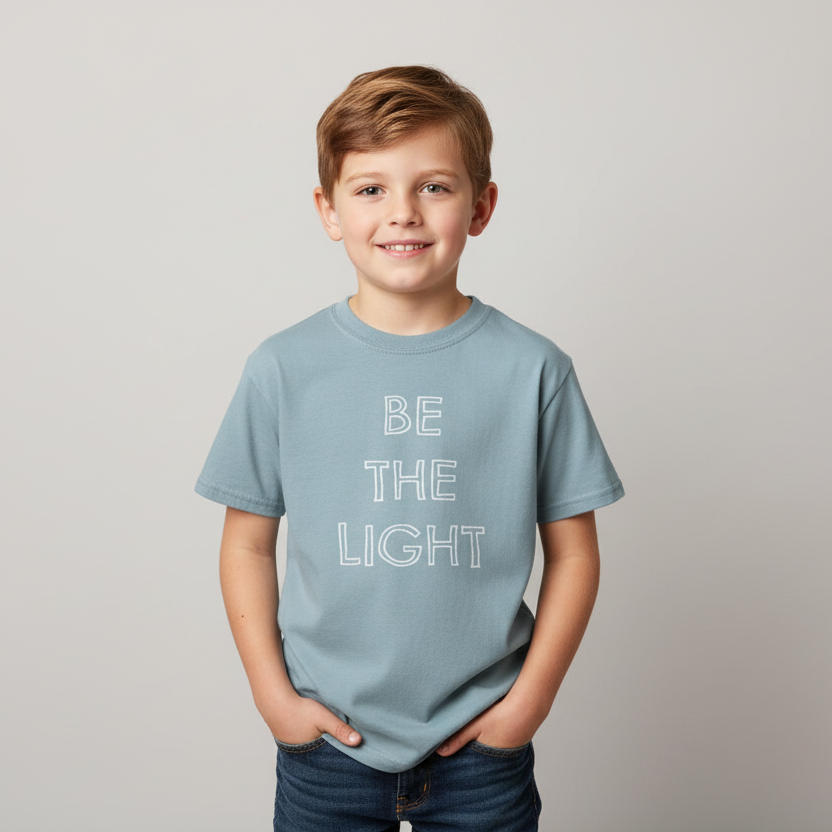 Light blue t-shirt with the phrase BE THE LIGHT written in white on the front center of the garment, with each word stacked above the other.