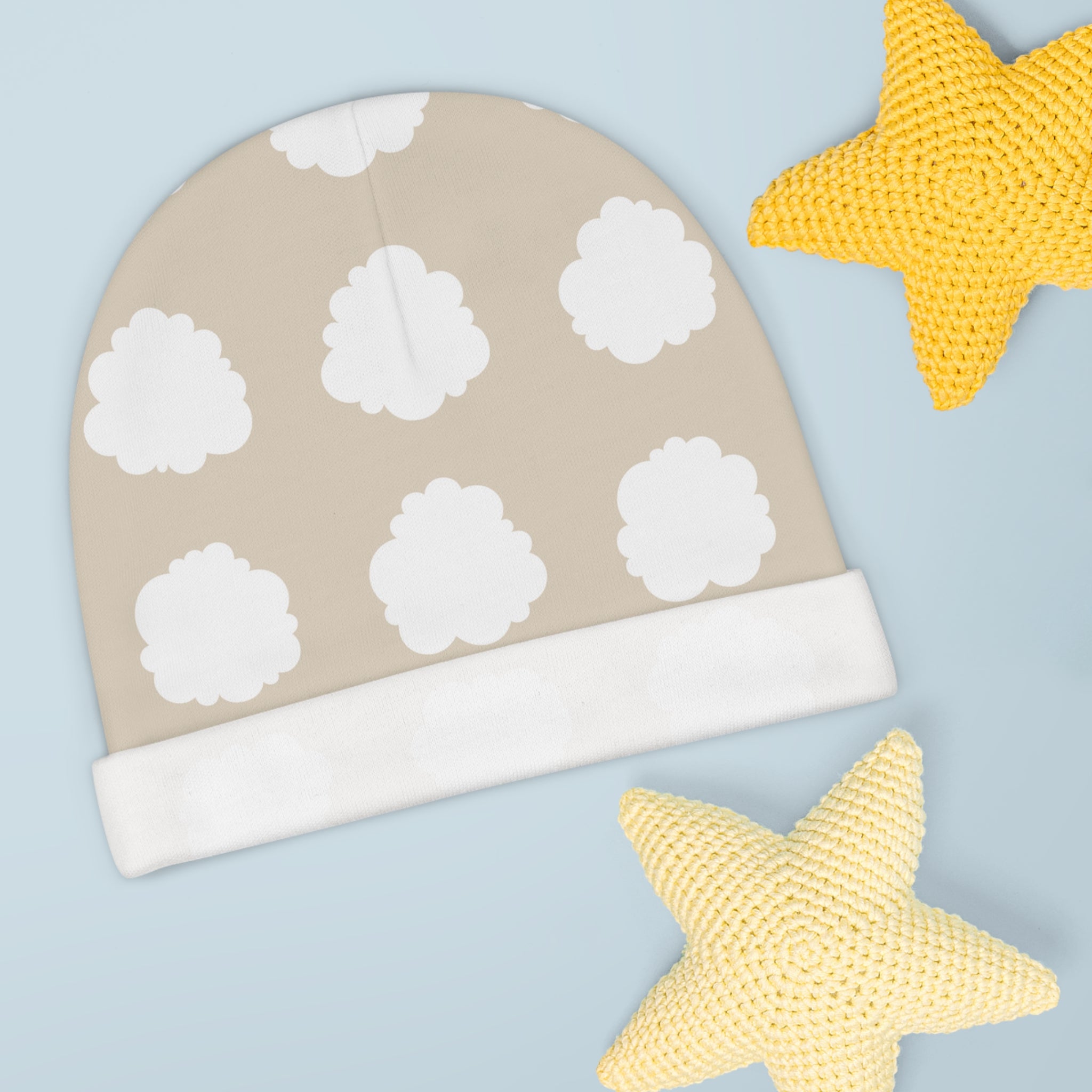 Beige baby hat with white cloud patterns and yellow star toys on a light blue background