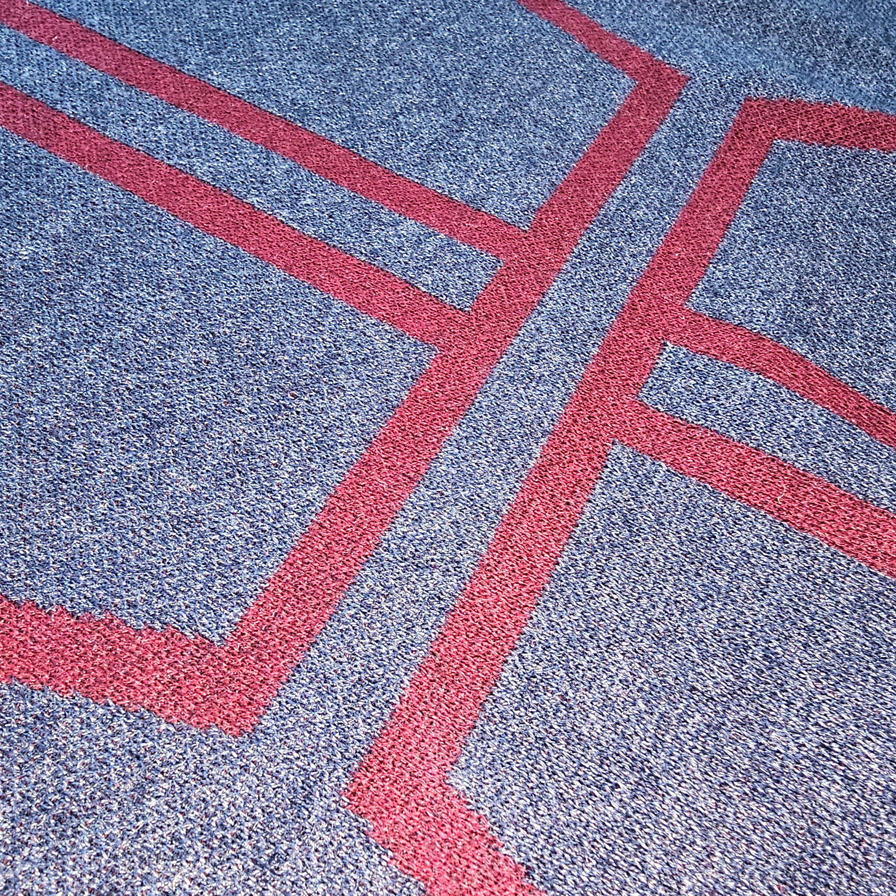 An angled close-up of the burgundy knitted cross graphic on the sweater chest.
