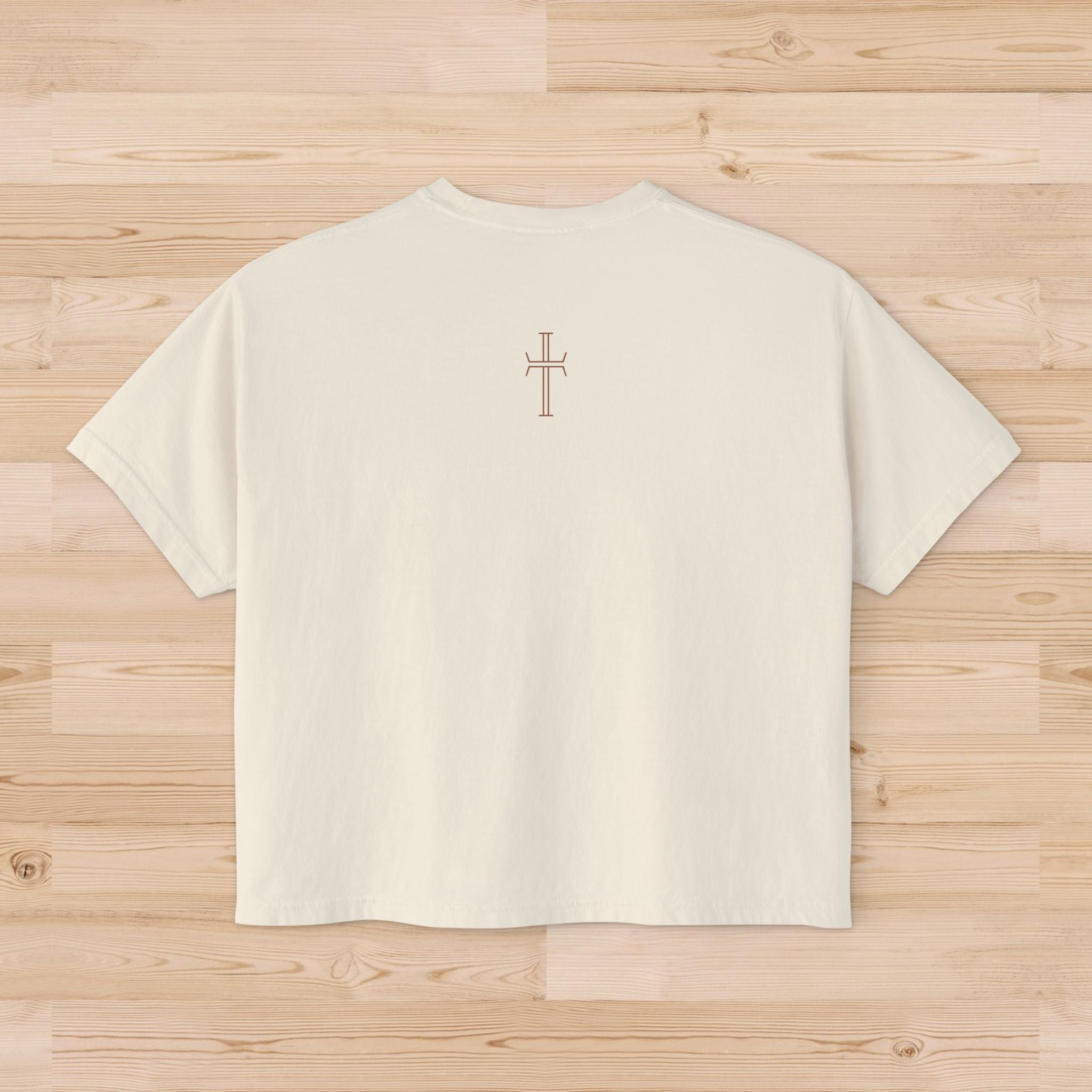 Beige t-shirt with a light brown cross on the upper back against a wooden surface
