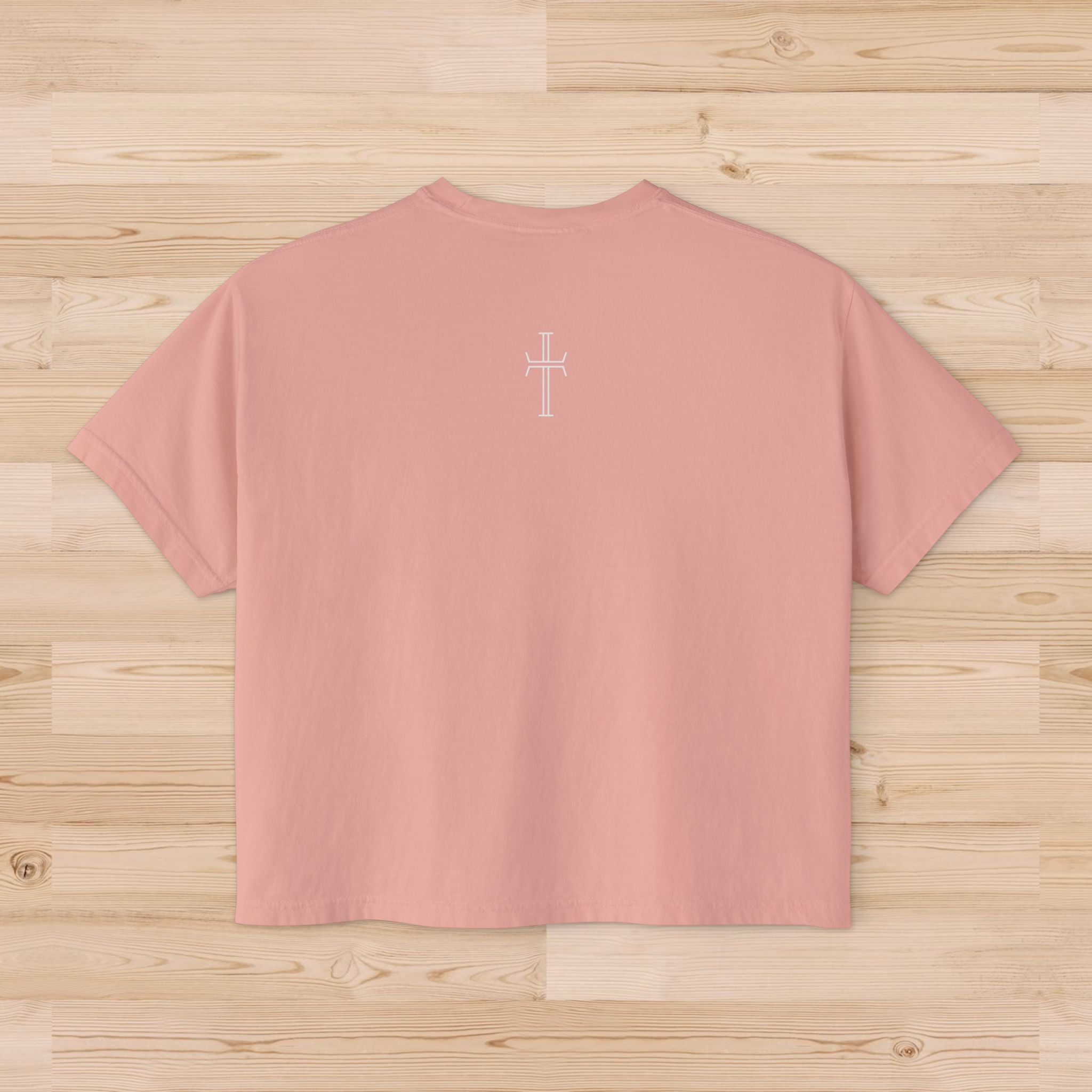 Peach-colored t-shirt with a white cross design on the upper back against a wooden surface
