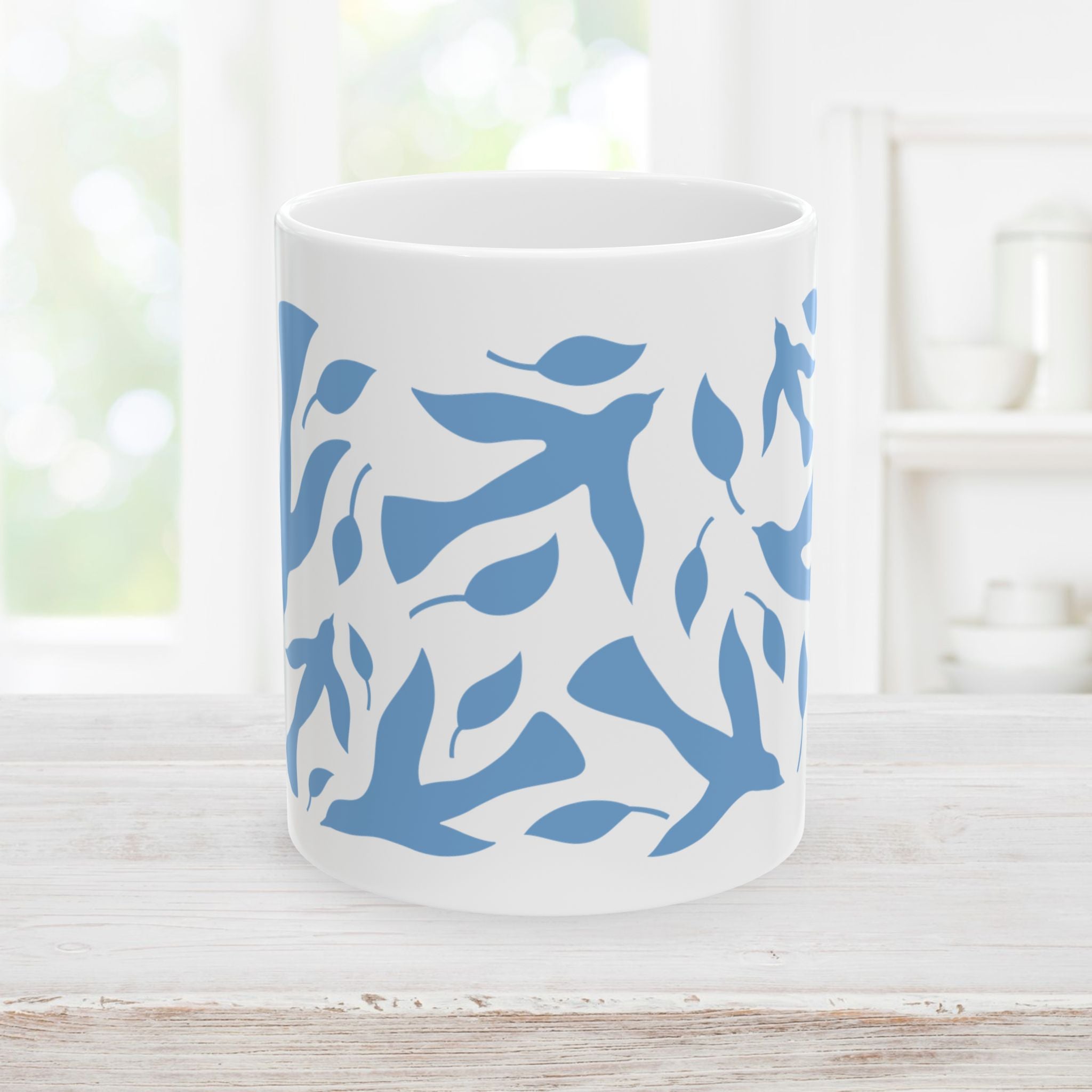 White ceramic mug with blue dove and leaf pattern on a wooden surface