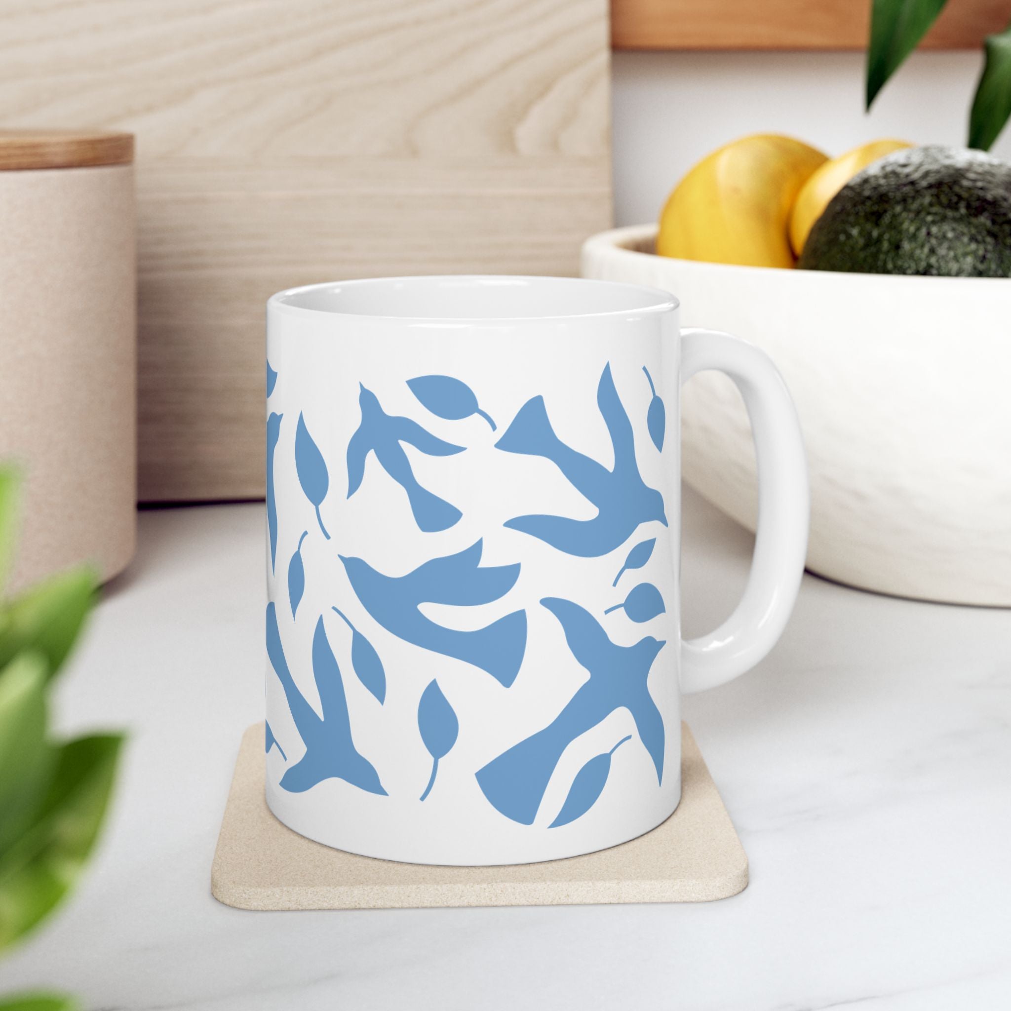 11oz white mug with blue dove and leaf pattern on a kitchen counter with a bowl of fruit in the background