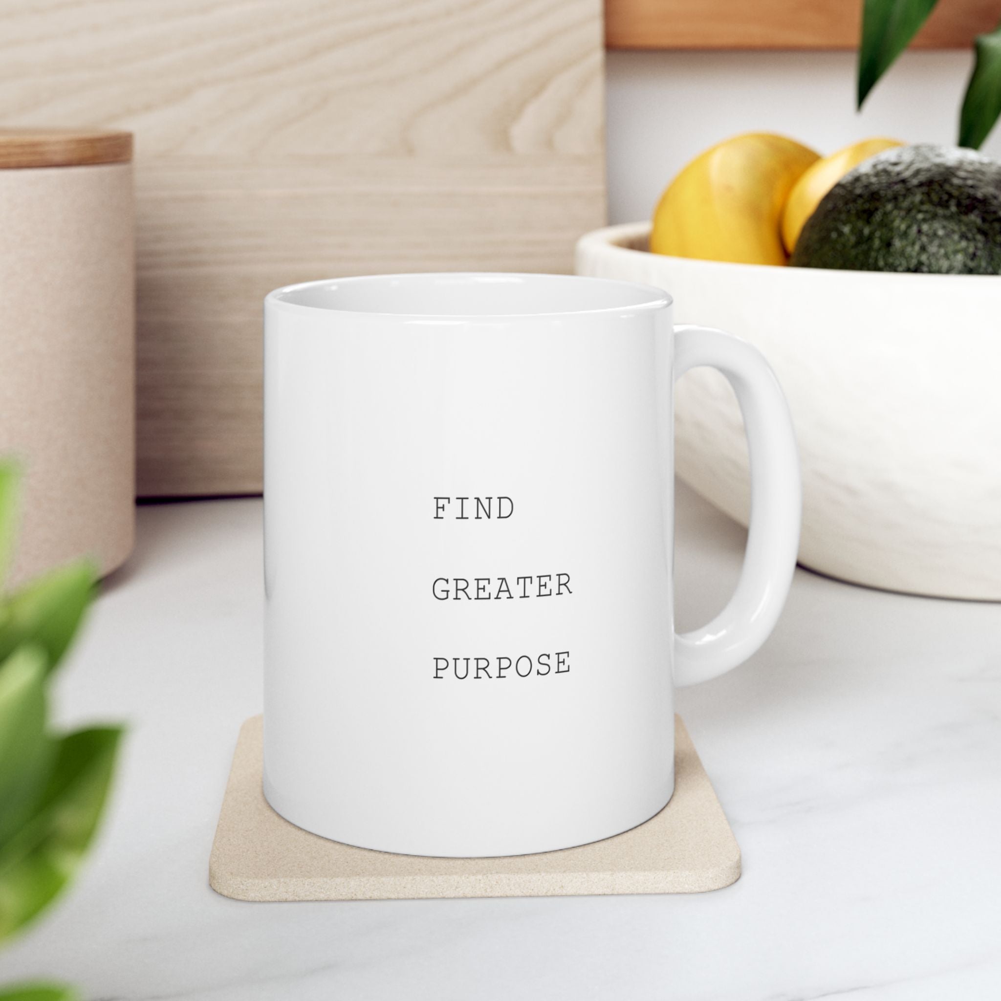White mug with 'Find Greater Purpose' text on a coaster, surrounded by plants and a bowl of fruit.