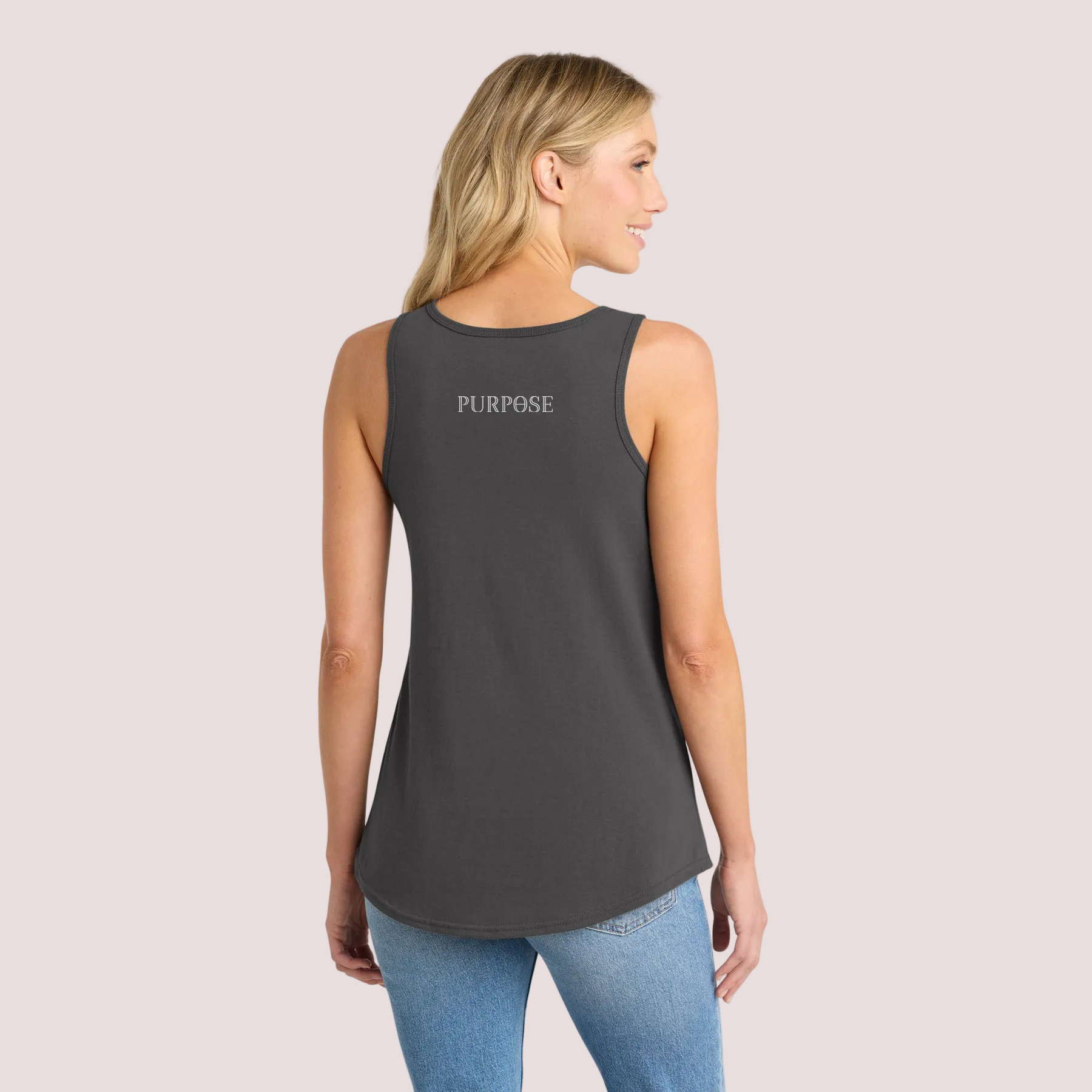 Woman wearing a dark gray tank top with the word 'PURPOSE' on the upper back and blue jeans on a pale background
