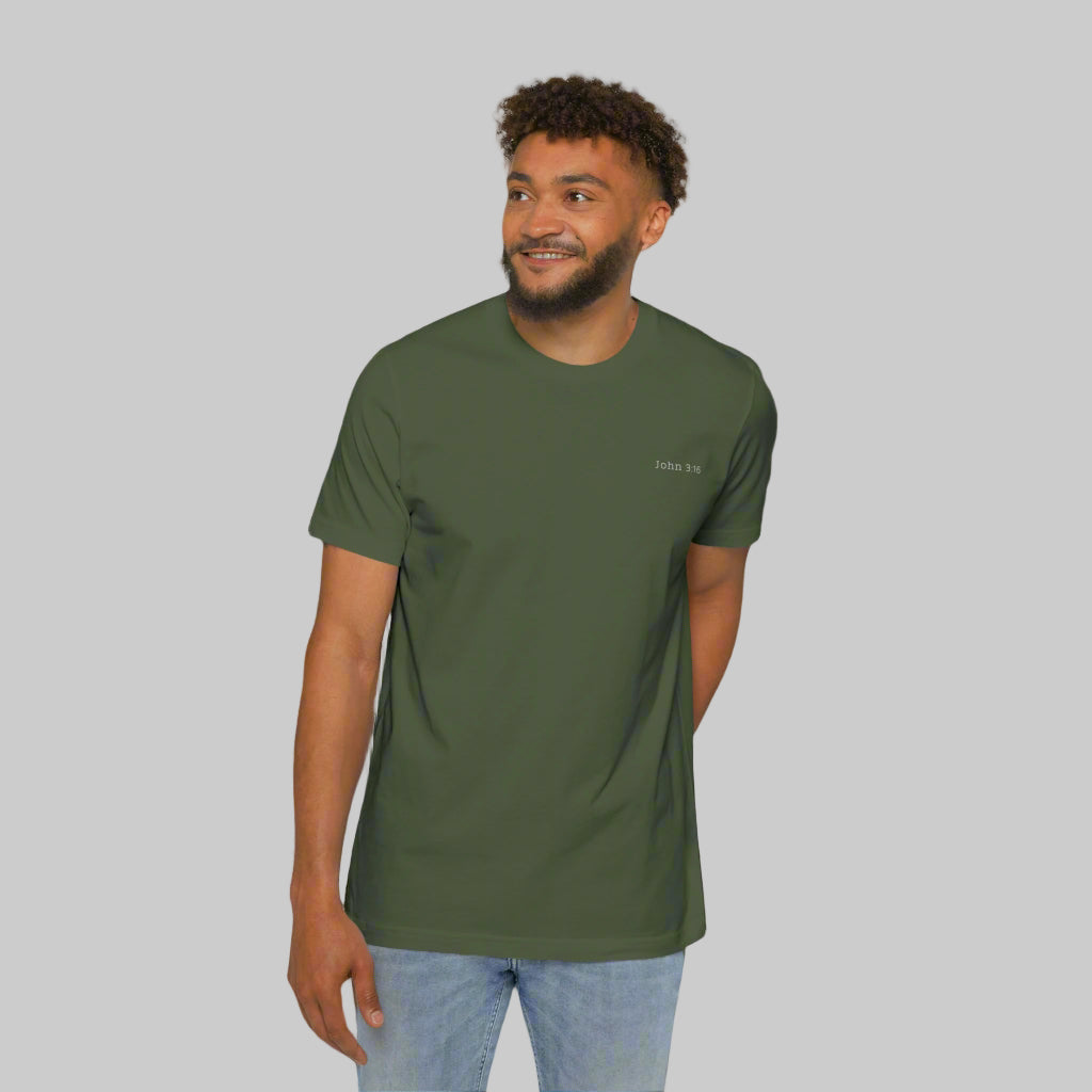 The front side of a male model wearing blue jeans and an army green tee shirt with the bible verse John 3:16 written in white on the left chest.