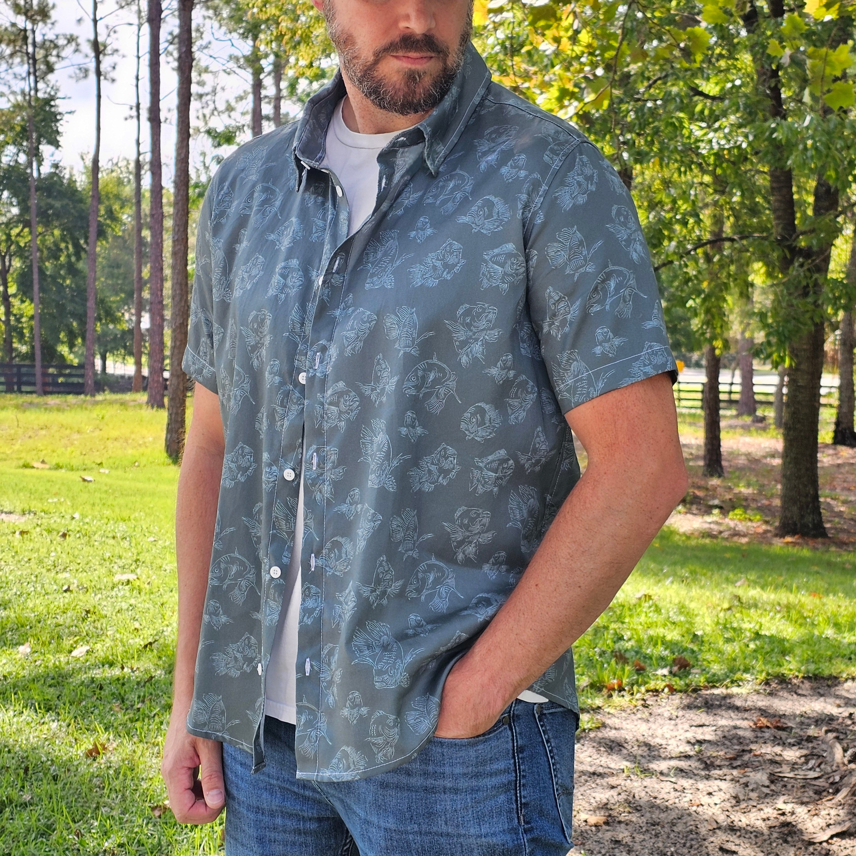 Man wearing a patterned shirt and cap outdoors with trees in the background