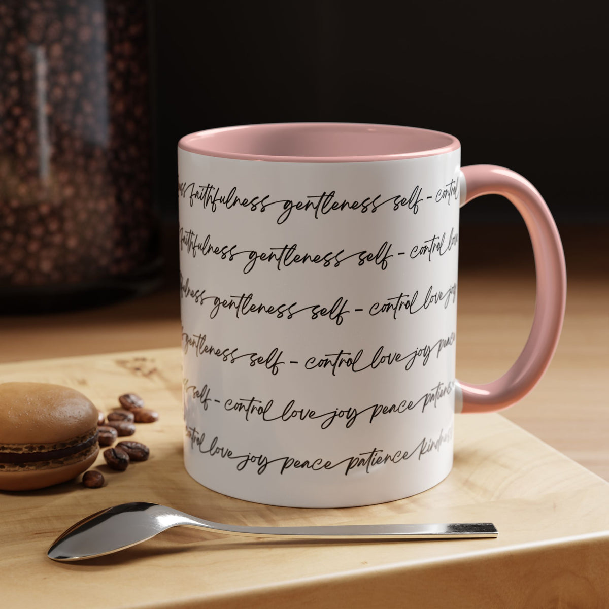Right side of 11oz mug with pink interior and handle with black scripted text written on a white background sitting on a wooden surface with coffee beans and a spoon.