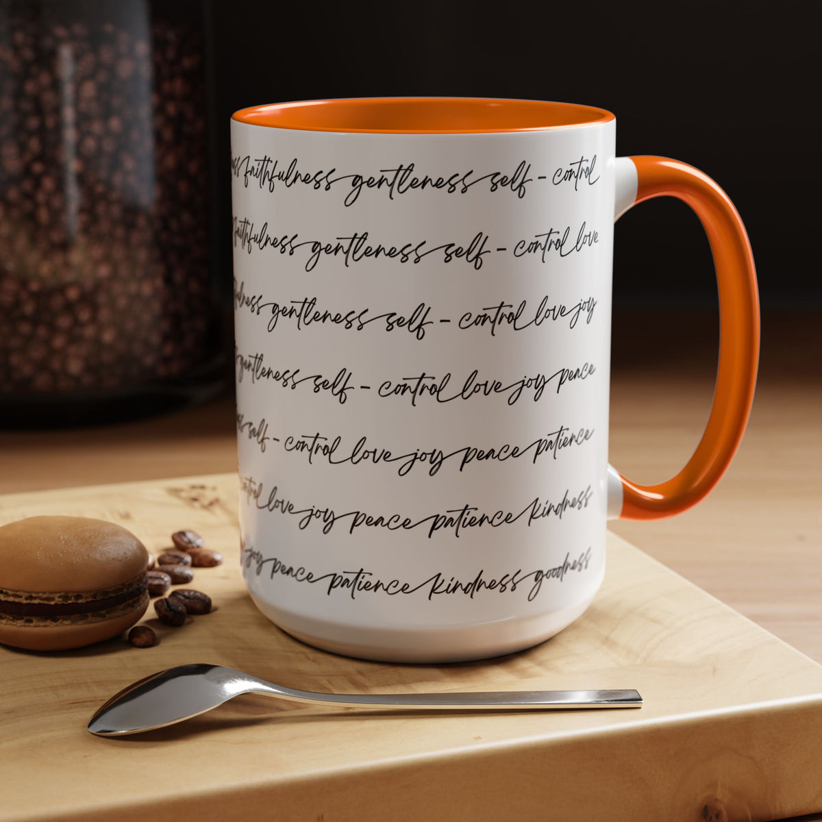 Right side of 15oz mug with orange interior and handle with black scripted text written on a white background sitting on a wooden surface with coffee beans and a spoon.