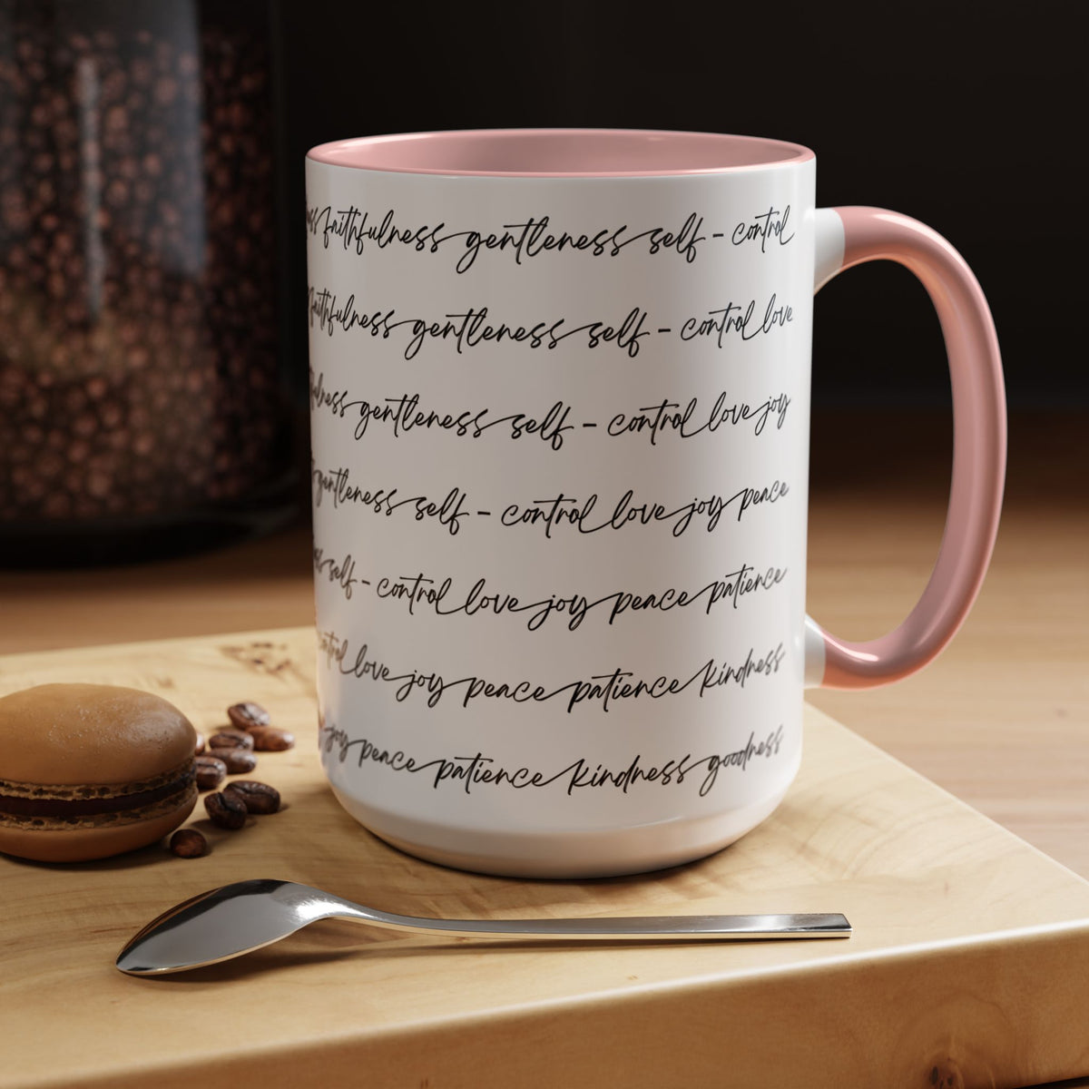 Right side of 15oz mug with pink interior and handle with black scripted text written on a white background sitting on a wooden surface with coffee beans and a spoon.