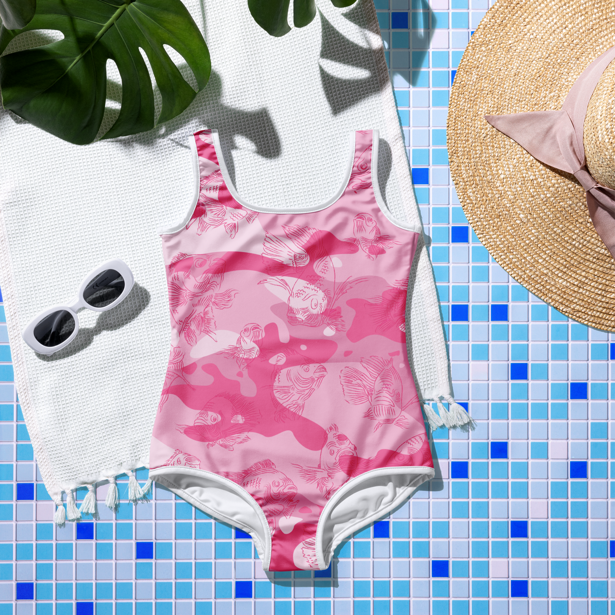 Pink swimsuit with pink camo and fish print on a blue tiled surface, accompanied by a hat and sunglasses.