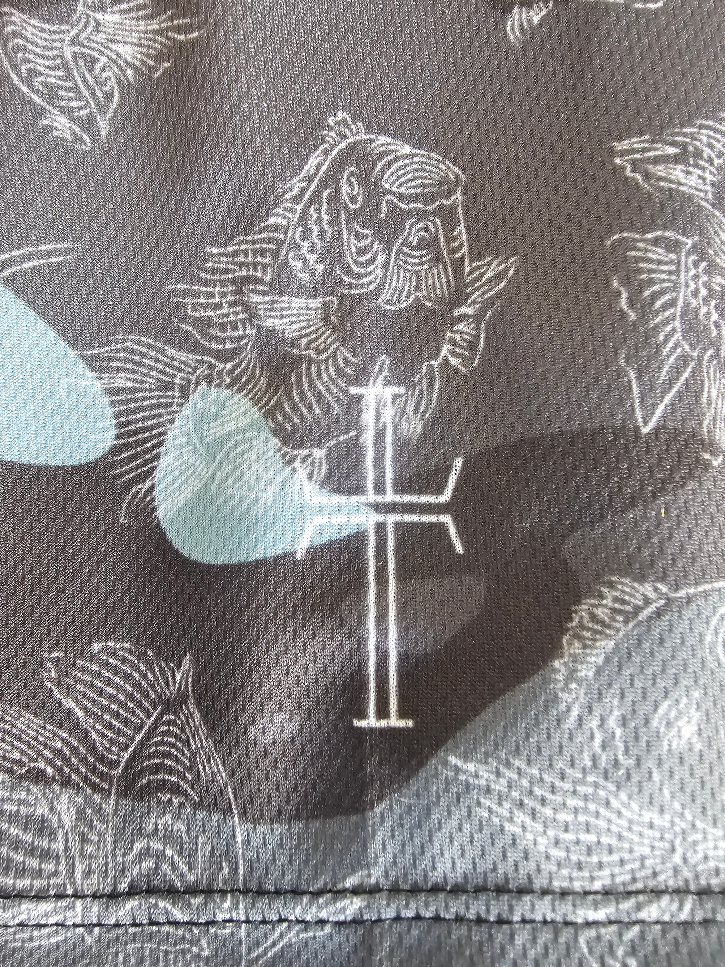 Close-up of the left sleeve with a white cross logo against a dark gray, black, and blue camo patterned fabric with white carp graphic illustrations.