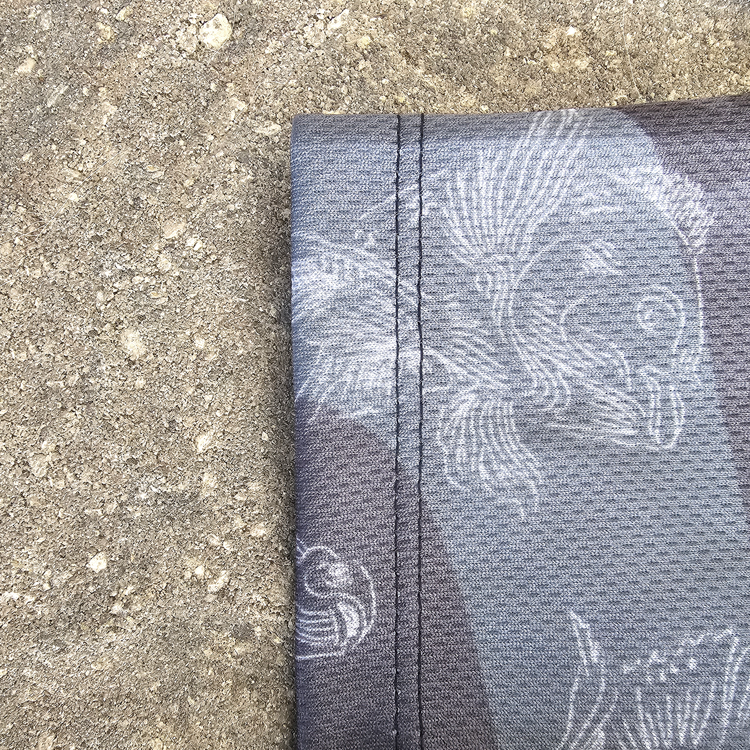 A close-up of the right sleeve stitching in a dark gray, black, and blue camo fabric with a white carp pattern, laid flat on a textured concrete surface.