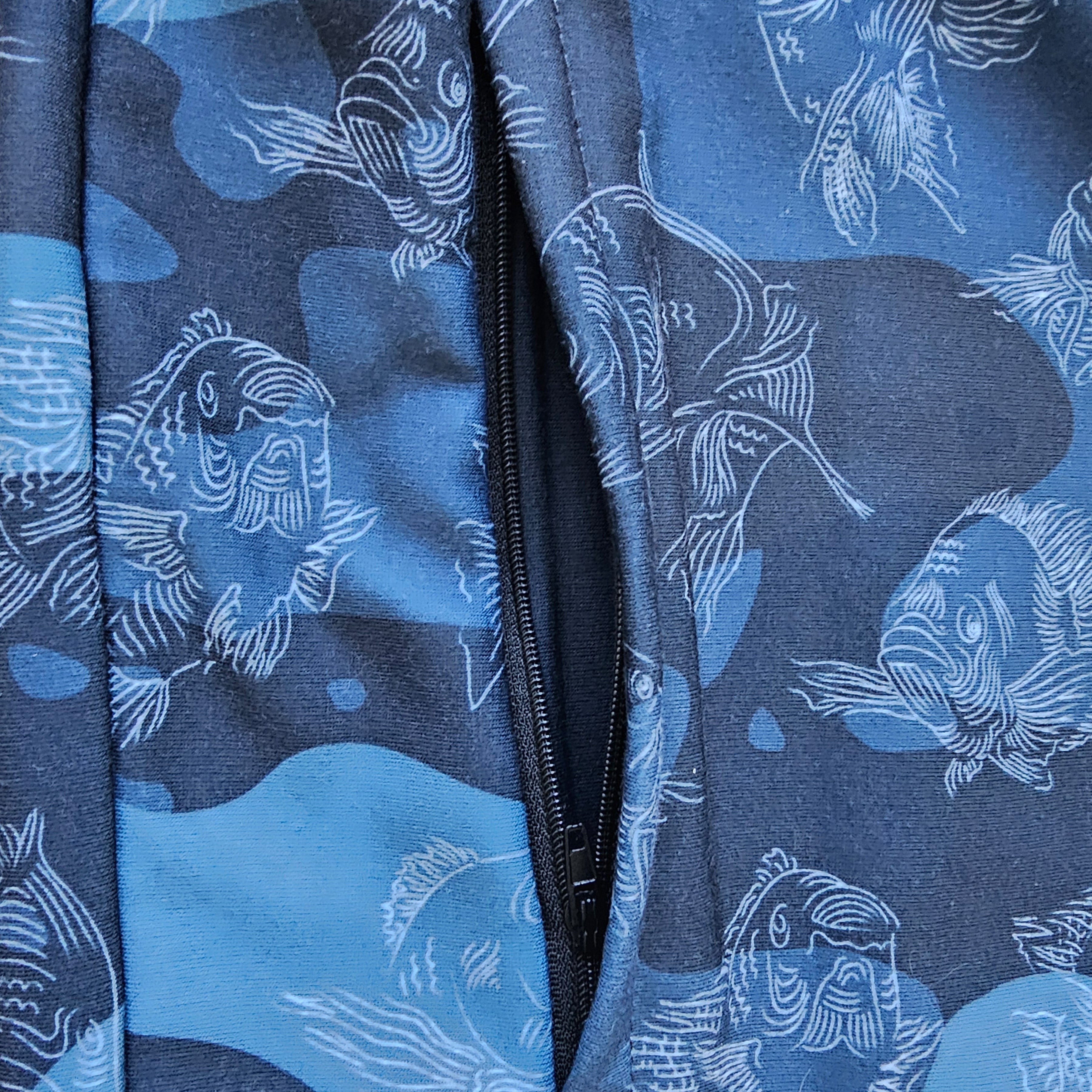 Close-up of the hidden zipper pocket of a a blue camouflage track jacket with fish pattern on a blue background