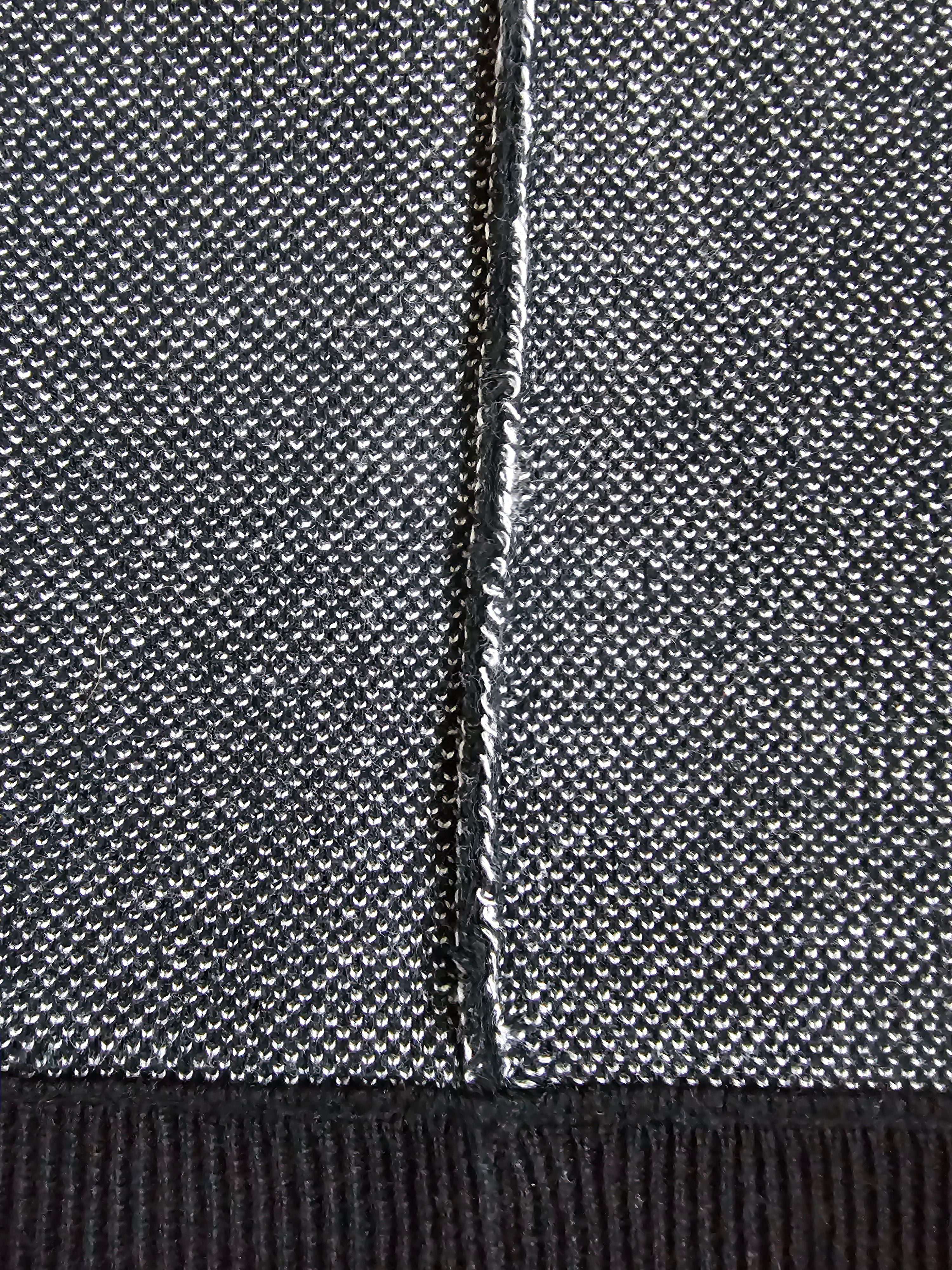 Close-up of a textured knit fabric in a heathered gray and black colorway, showing a central seam and a ribbed black hem.
