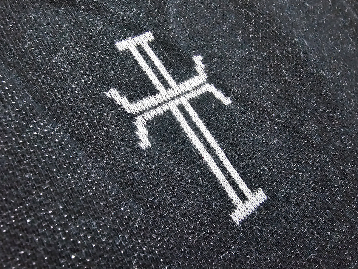 Close-up of a black knit fabric with a white knit stylized cross.
