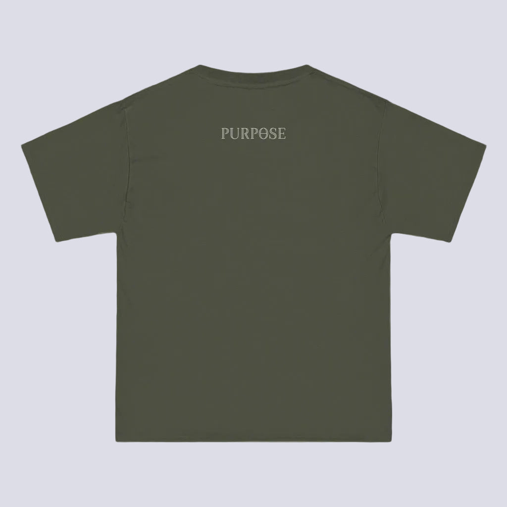 A roomy army green crewneck tee shirt displays the back of the garment as it lays against a painted brick-patterned wall. The Purpose worded logo is printed in white along the top center.