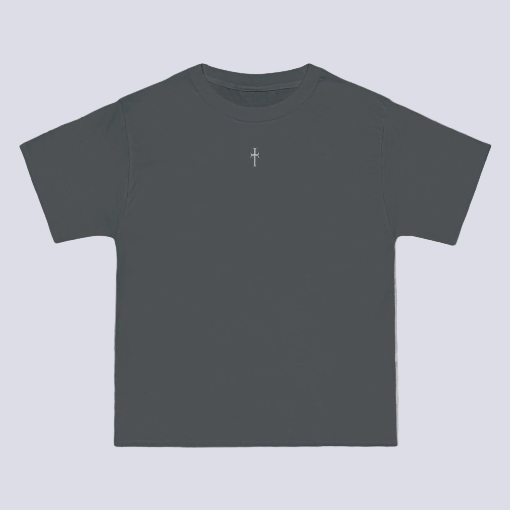A gray crewneck tee shirt displays the front of the garment as it lays against a brick-patterned wall. A small white Purpose cross logo is printed at the top center.