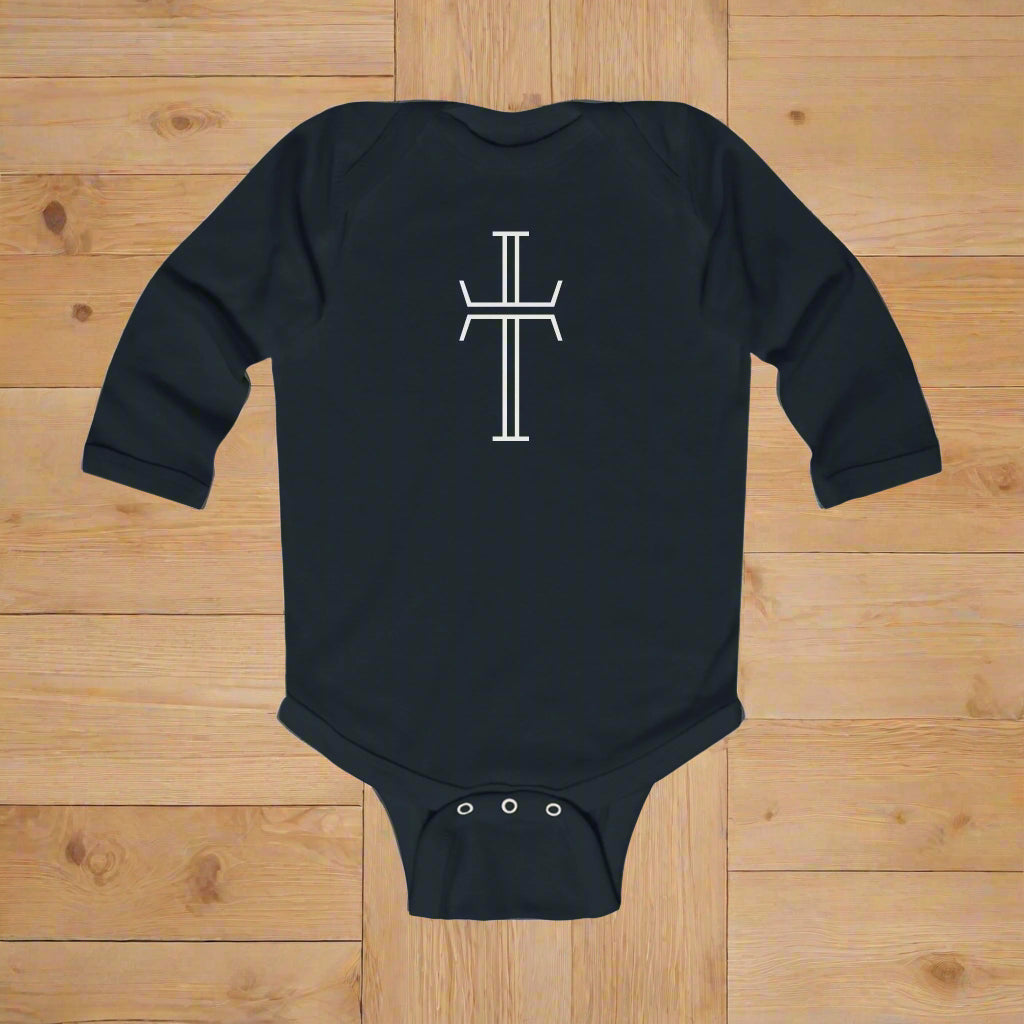 Black baby onesie with a white crucifix symbol on a wood floor background