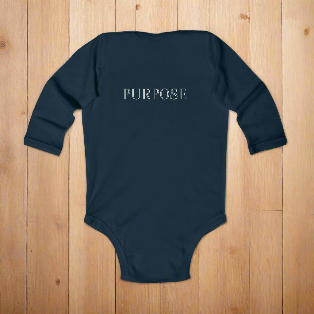 Navy blue baby onesie with 'PURPOSE' printed on the back laying on a wood floor