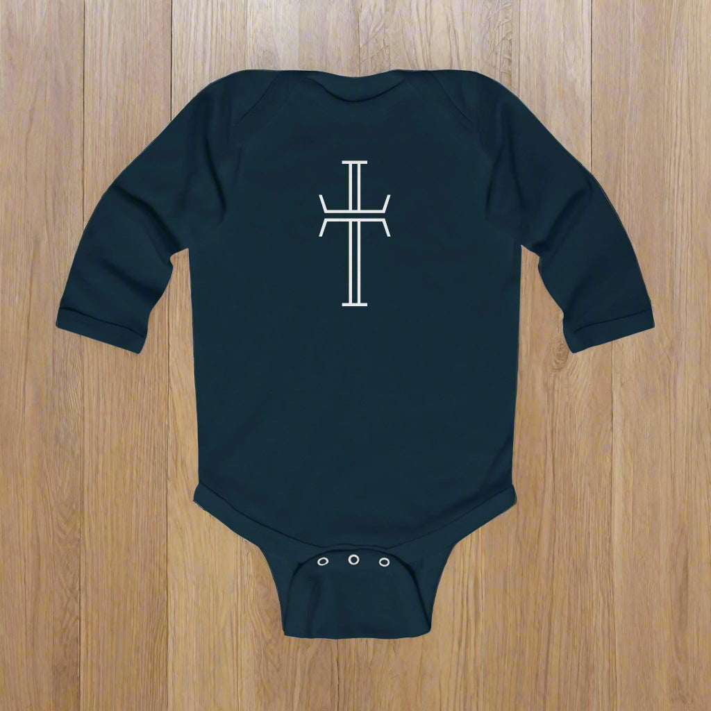 Navy blue baby onesie with a white crucifix on the back against a wood floor