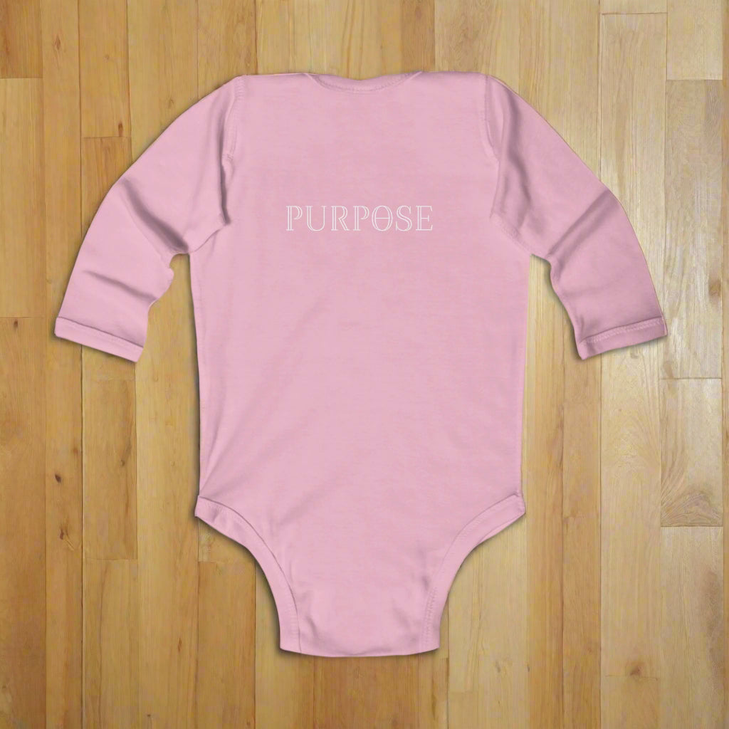 Pink baby onesie with 'PURPOSE' text on a wood floor