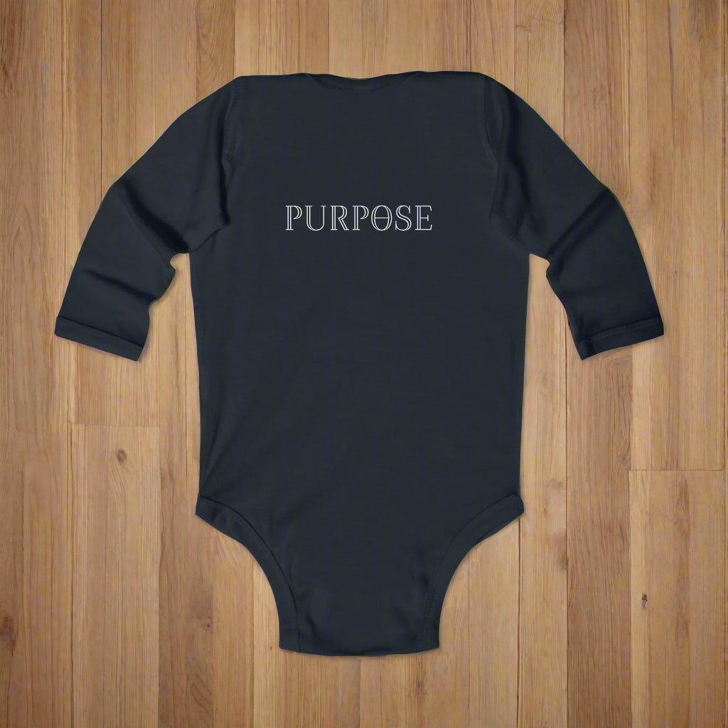 Black baby onesie with 'PURPOSE' printed on the back laying on a wood floor