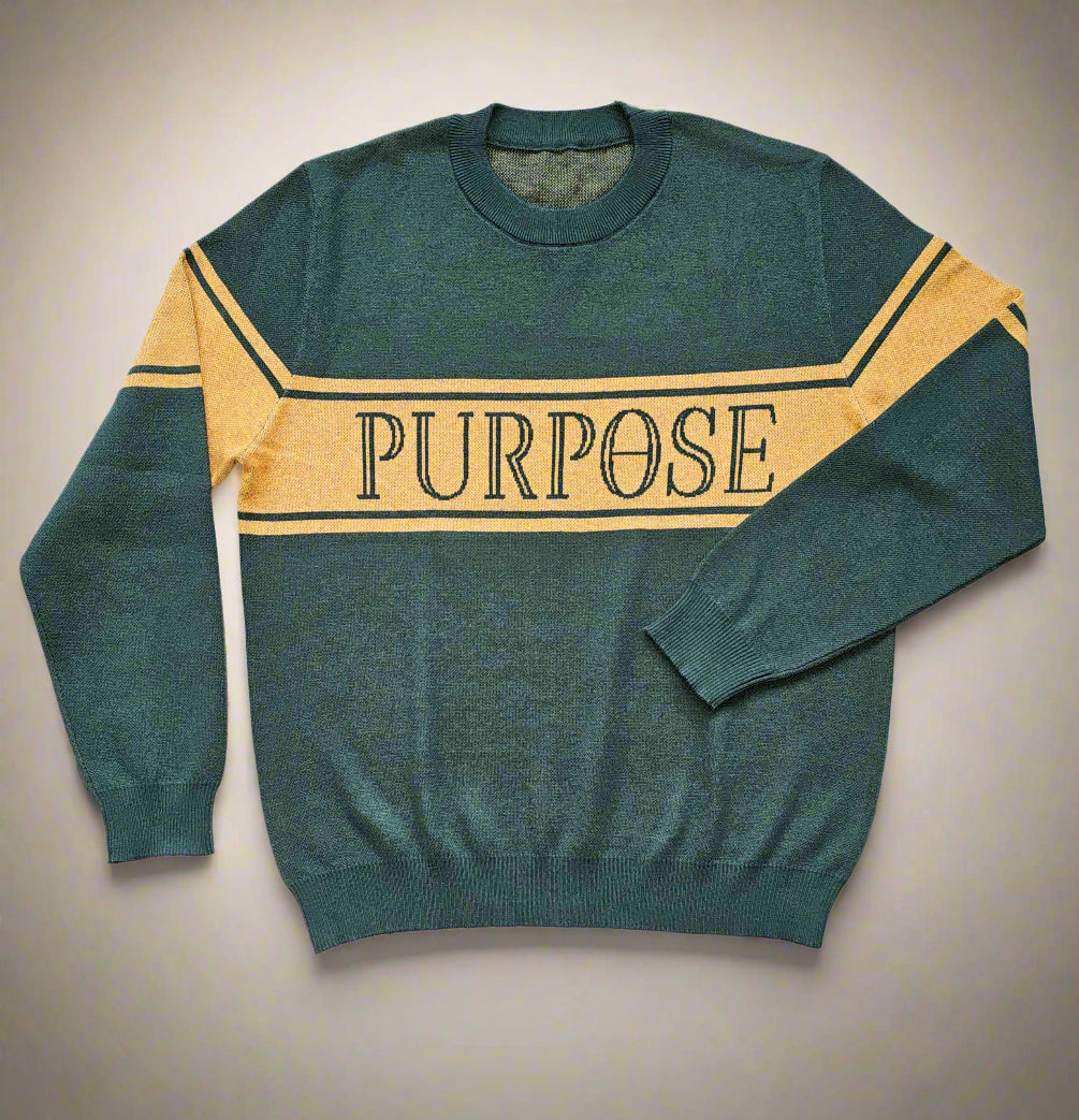 The forest green sweater is laying against a white background. The three mustard-colored stripes across the center chest and upper arms are displayed. The word "Purpose" in forest green capital letters on the center of the chest is depicted.
