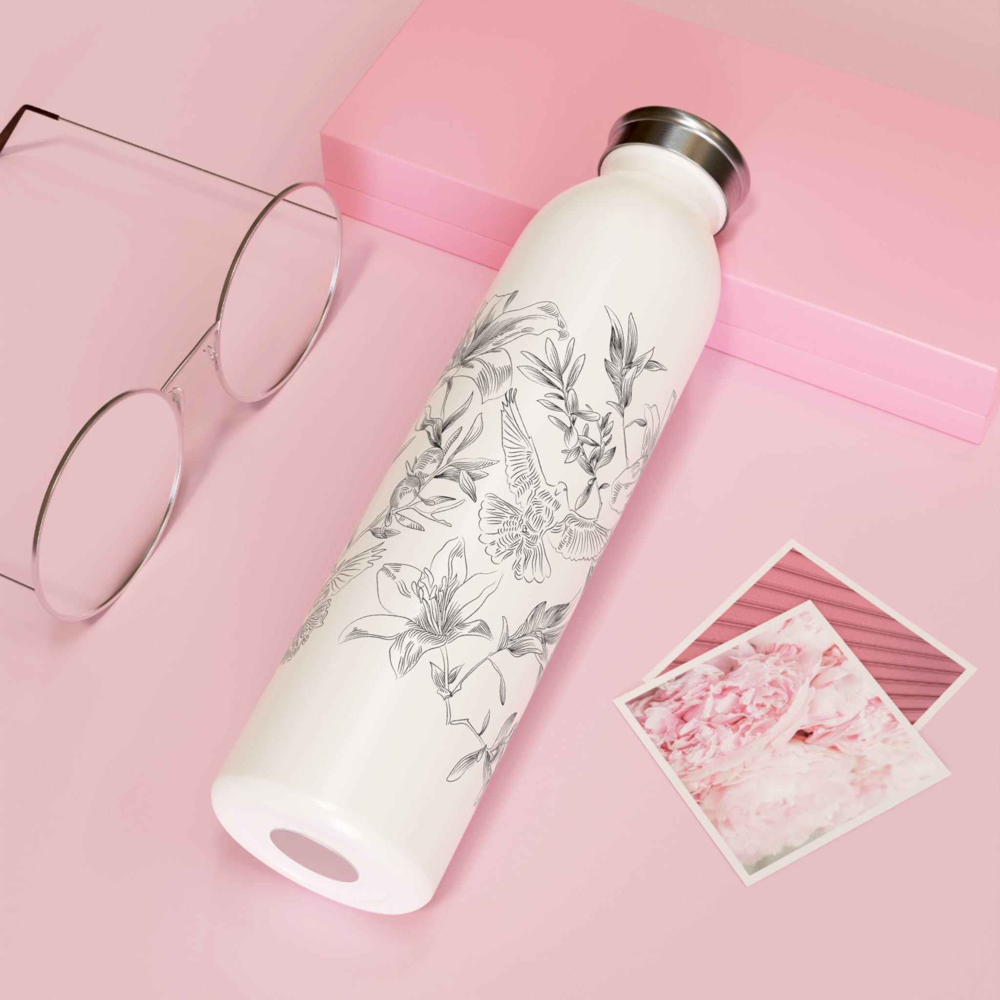 White water bottle with floral and dove design on a pink surface with glasses and postcards.
