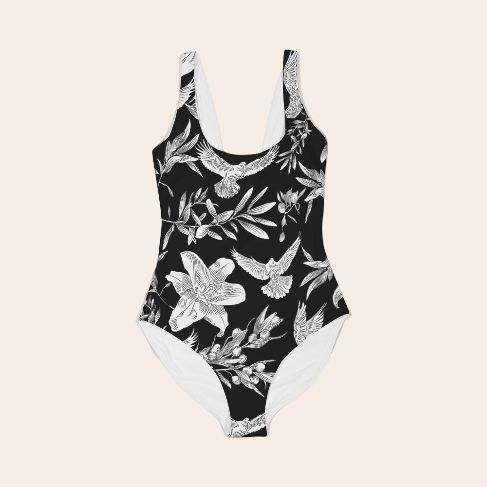 Black swimsuit with white floral and bird pattern laying flat against a white background