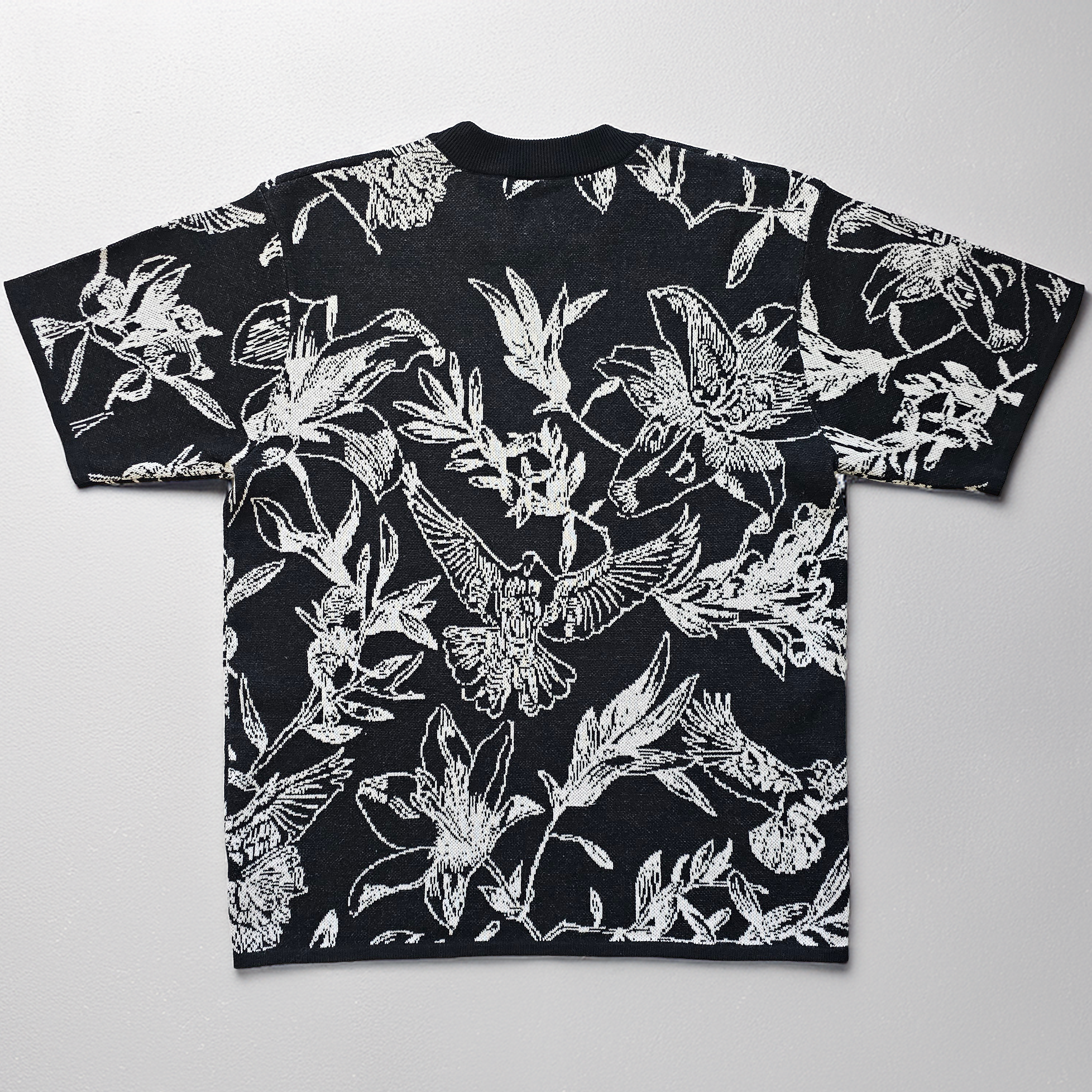 Black knitted t-shirt with white floral and dove pattern on a light gray background