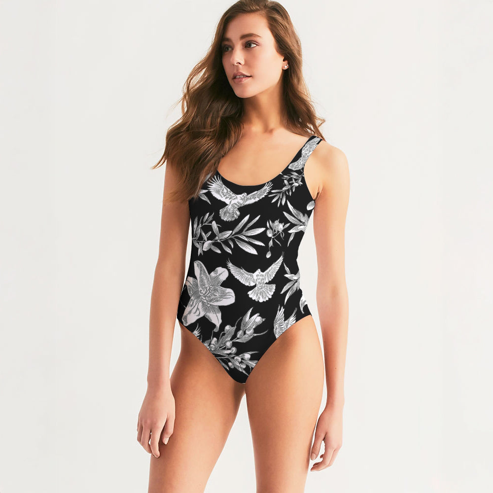 Front of woman wearing a black one-piece swimsuit with white floral patterns on a light gray background