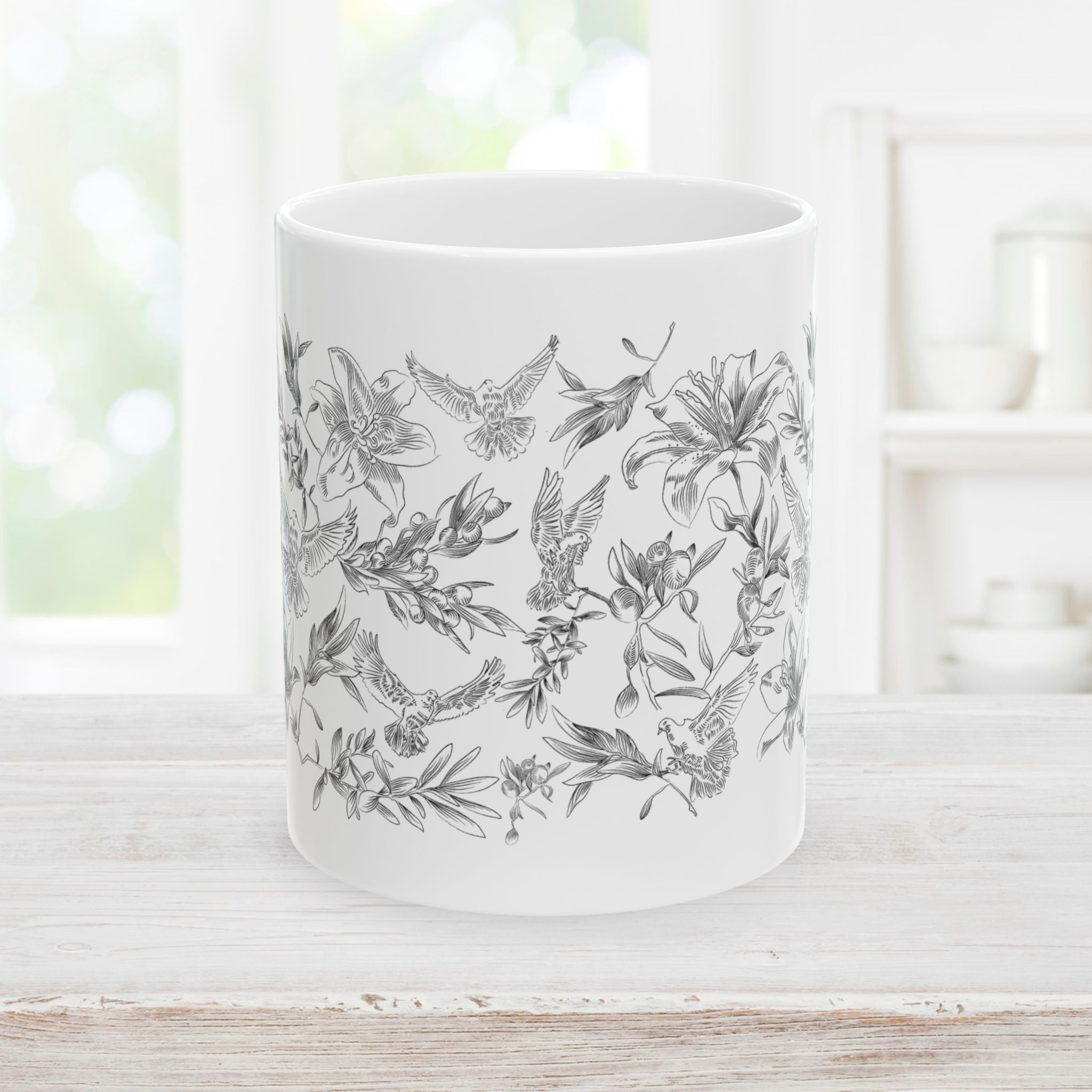 White mug with black floral and dove pattern on a wooden surface.