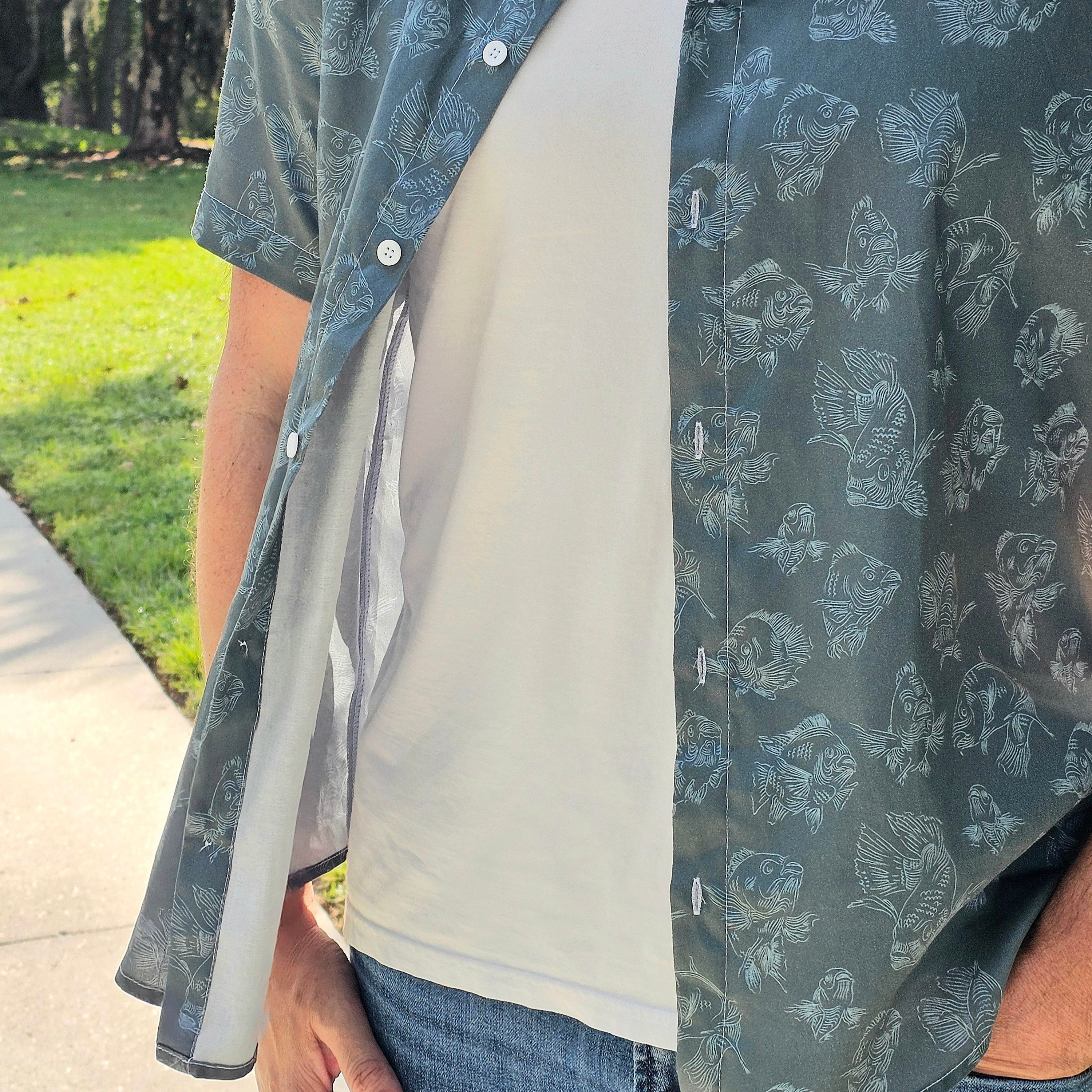 Person wearing a patterned shirt over a plain shirt with a grassy area in the background