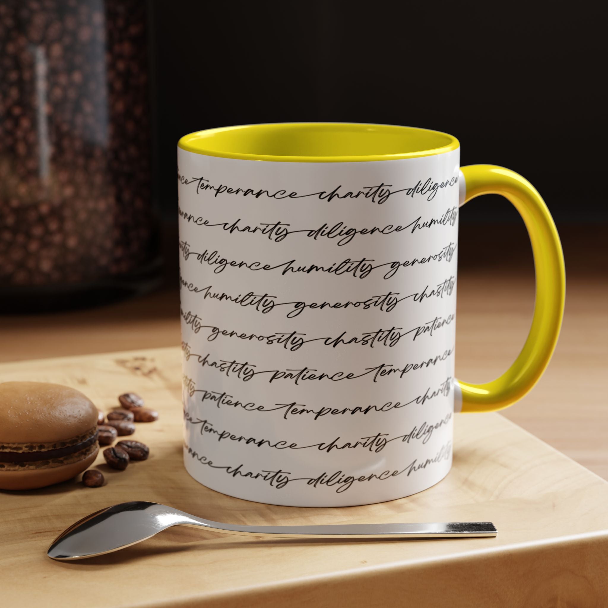White mug with the seven virtues scripted along the outside, with yellow interior and handle on a wooden surface with coffee beans and a spoon.