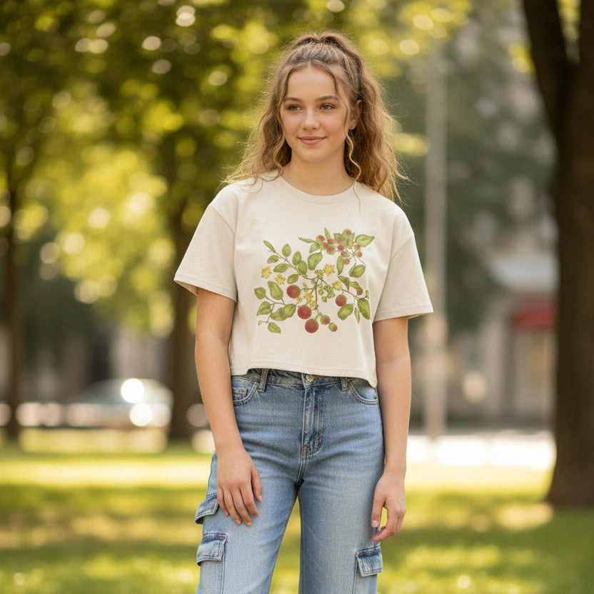 Teen girl wearing cropped t-shirt in a cream color with leaf, berry, and floral pattern on the front, cargo jeans, and sneakers in an outdoor setting. Christian t-shirt.