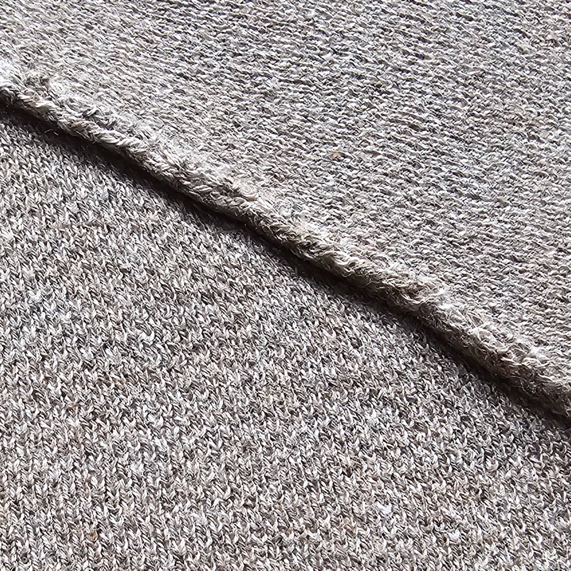 Close-up of gray textured fabric with a visible knit-finished seam.