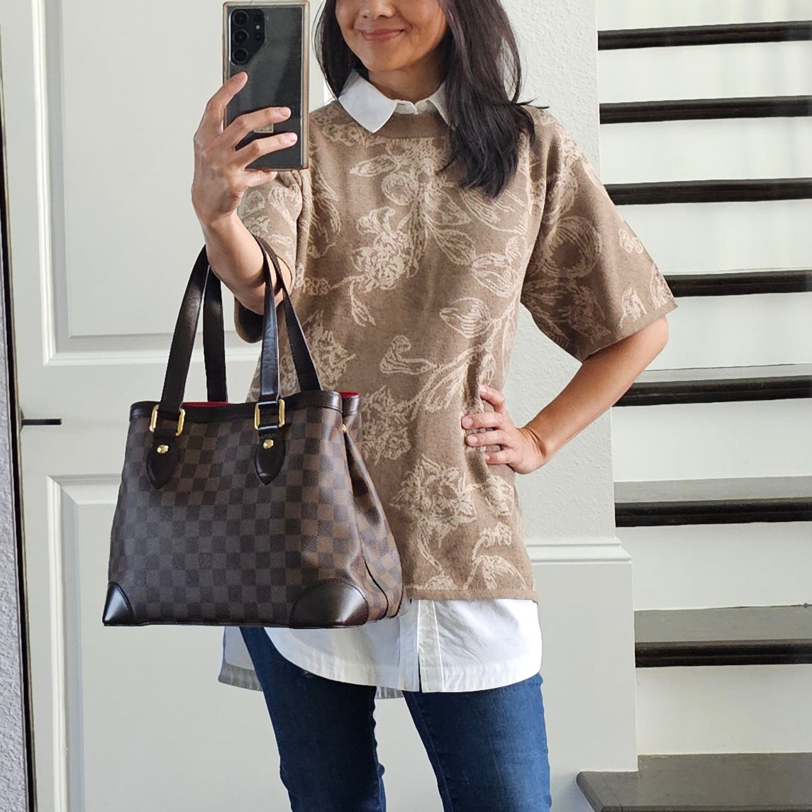 Person holding a brown checkered handbag in front of a white door.