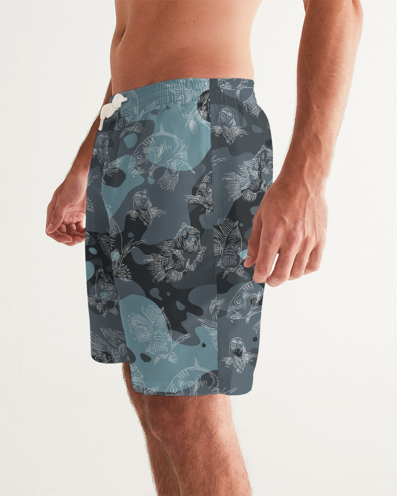 A left view close-up of a male model wearing a pair of blue camo board shorts with an all-over swimming carp print in a white pattern, with a white exterior drawstring loosely knotted.