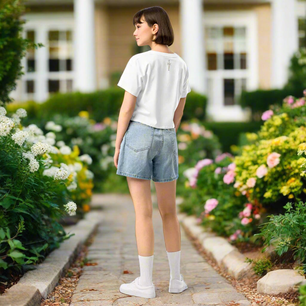 Woman in jeans and cropped t-shirt with an image of a beige colored crucifix at the center top