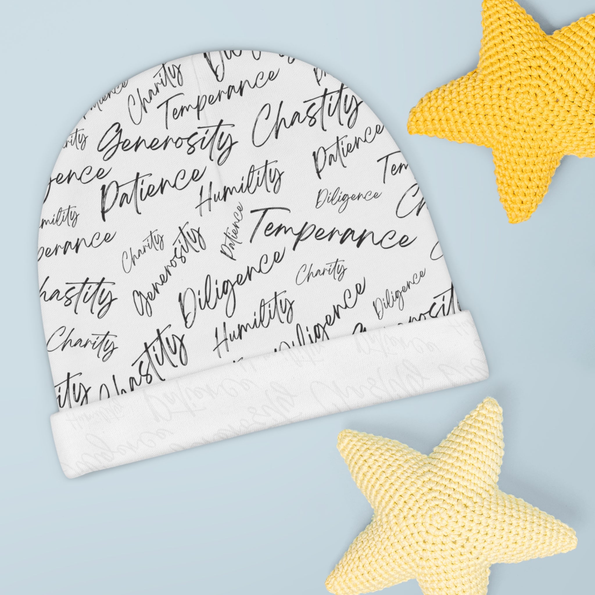 A white, knit, baby beanie with biblical virtues written in black script in a random all-over pattern on the cap, and a white, upturned brim.