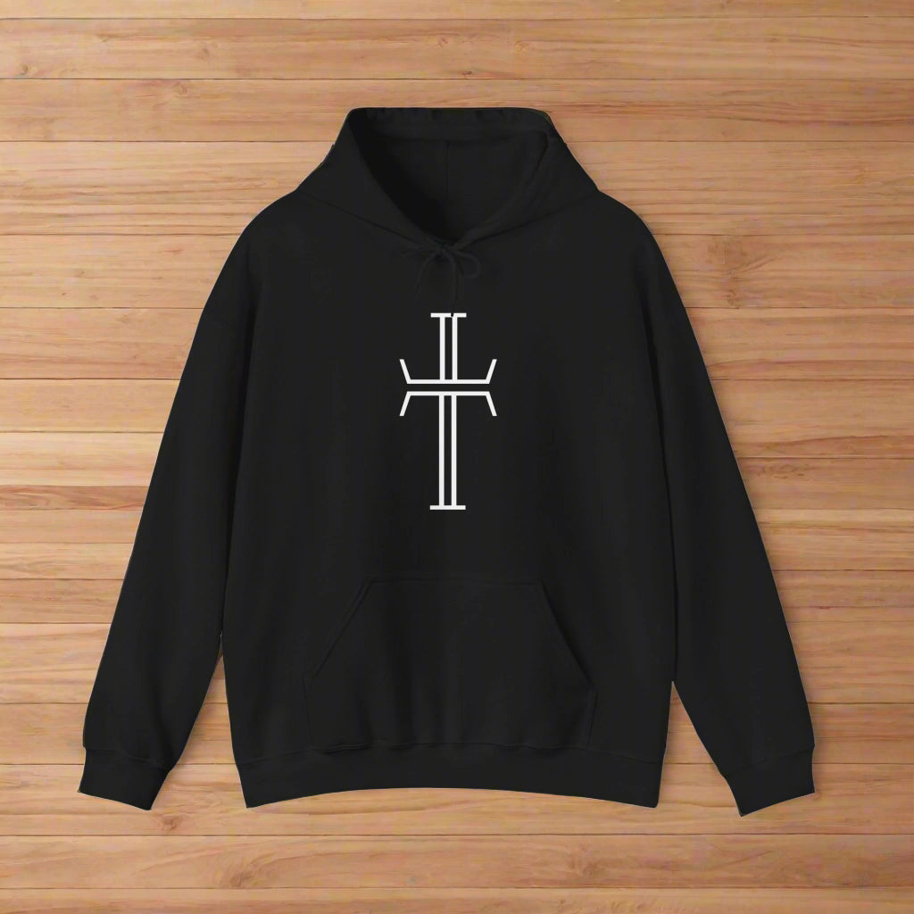 A black hoodie with a kangaroo pocket, lays against a wood floor, showing the front of the garment with the bold white Purpose cross logo across the chest.